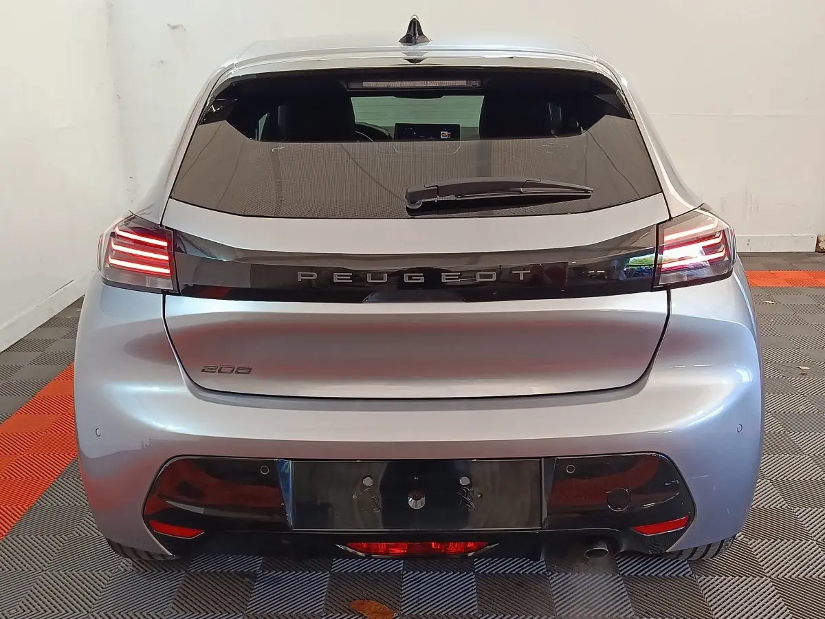 Vue arrière d'une Peugeot 208 gris clair 2025 avec feux LED et logo Peugeot lumineux sur la malle.