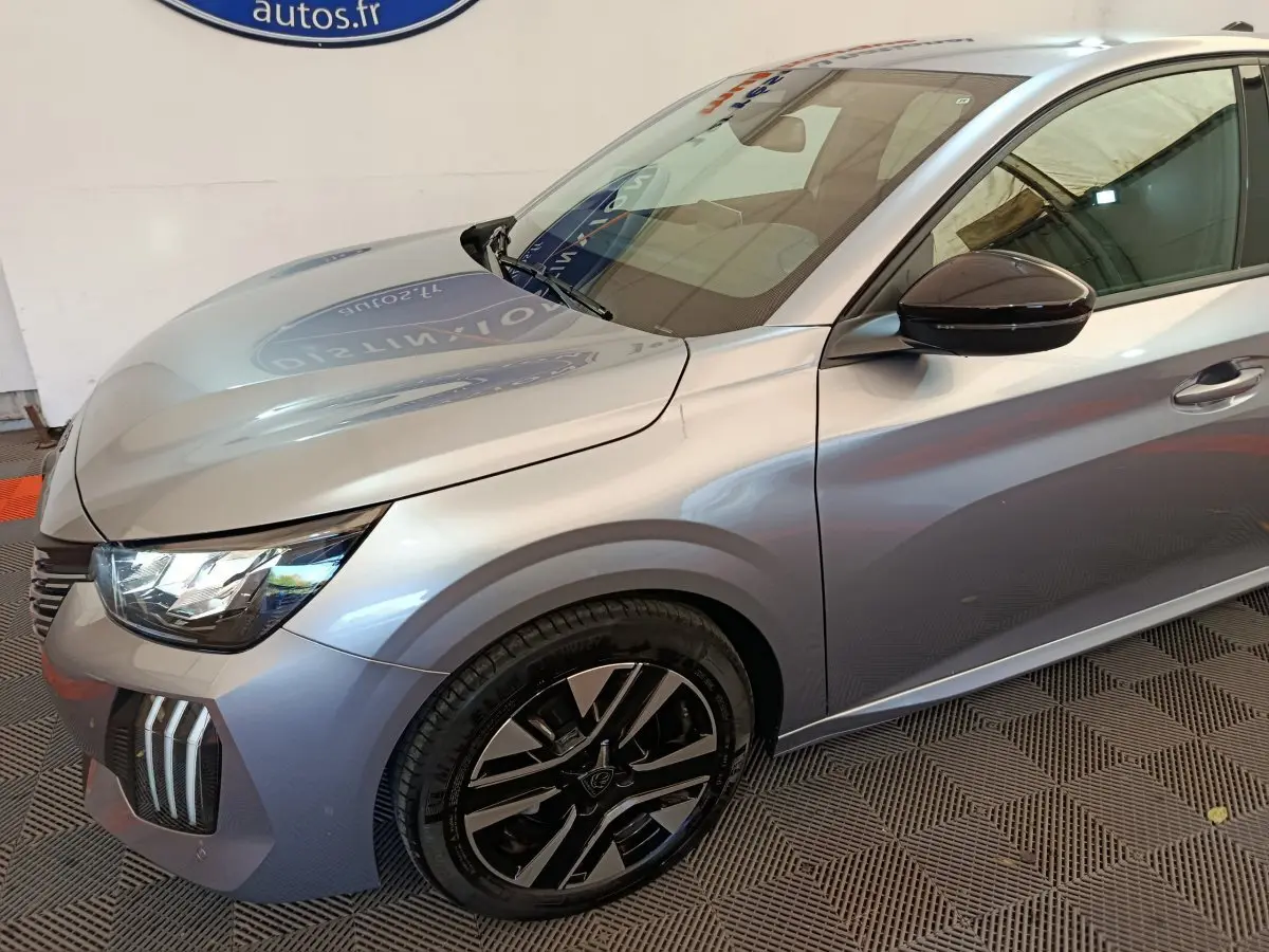 Vue 3/4 avant gauche d'une Peugeot 208 PureTech 100 S&S Allure gris clair avec jantes noires et rétroviseur noir.