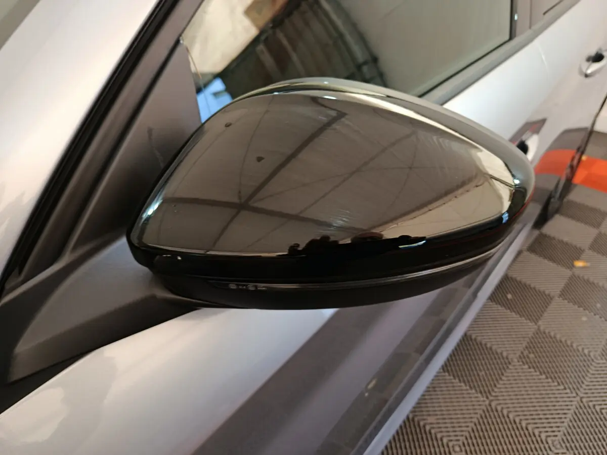 Rétroviseur noir côté gauche d'une Peugeot 208 gris clair, vue rapprochée en intérieur showroom.
