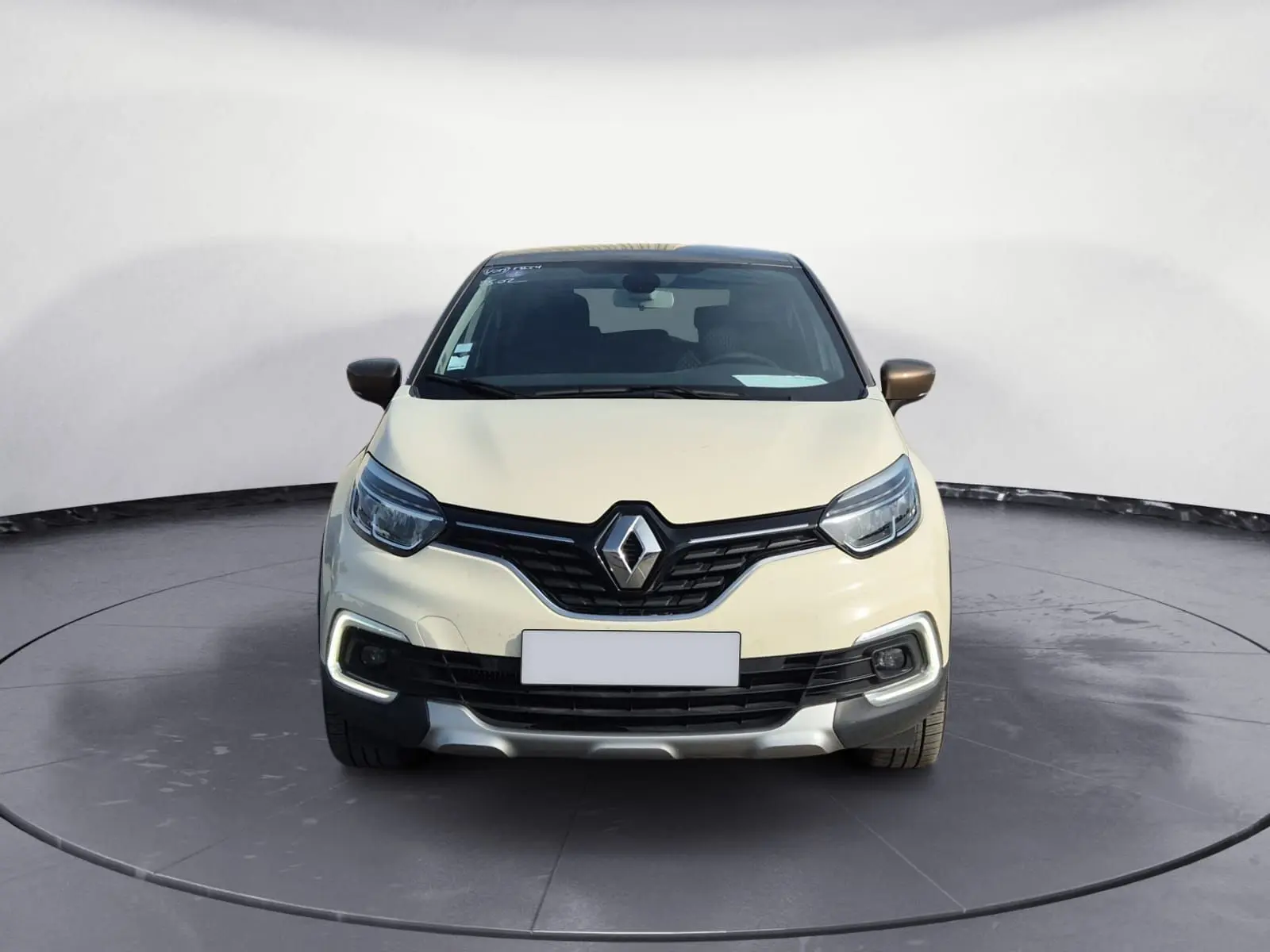 Vue frontale d'un Renault Captur beige et marron, mettant en valeur la calandre noire et les feux LED en forme de C.