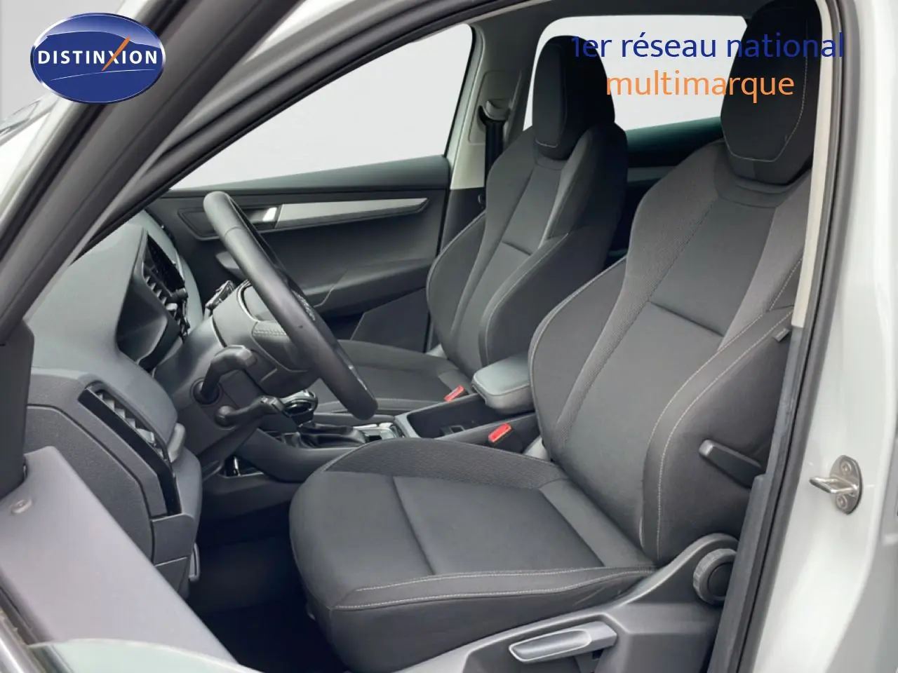 Vue intérieure côté conducteur du Skoda Karoq blanc glacier 2025, sièges en tissu noir avec volant multifonction.