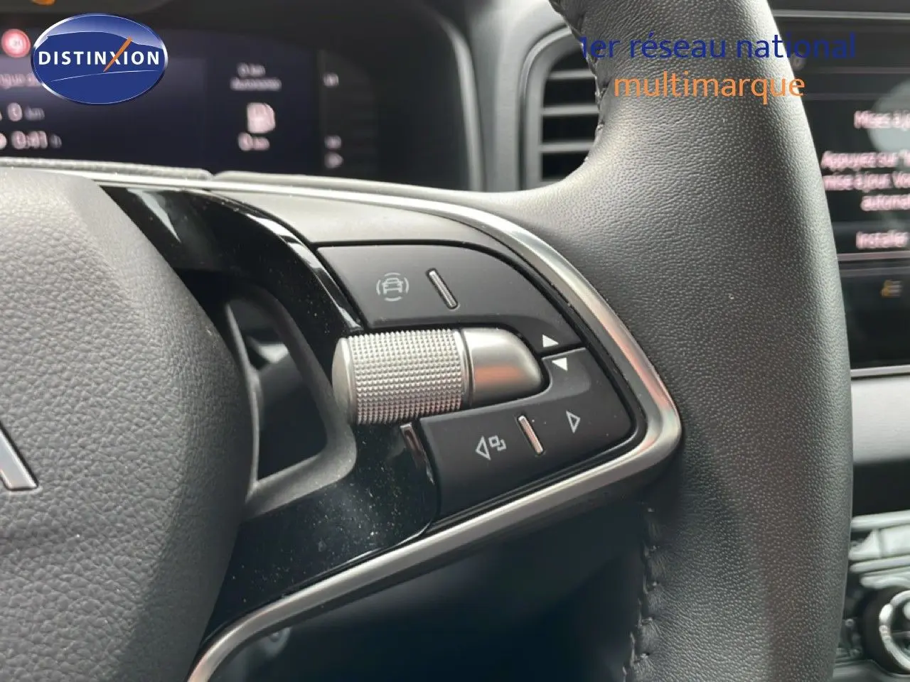Gros plan sur les commandes multifonctions du volant en cuir noir du Skoda Karoq blanc glacier, avec tableau de bord en arrière-plan flou.