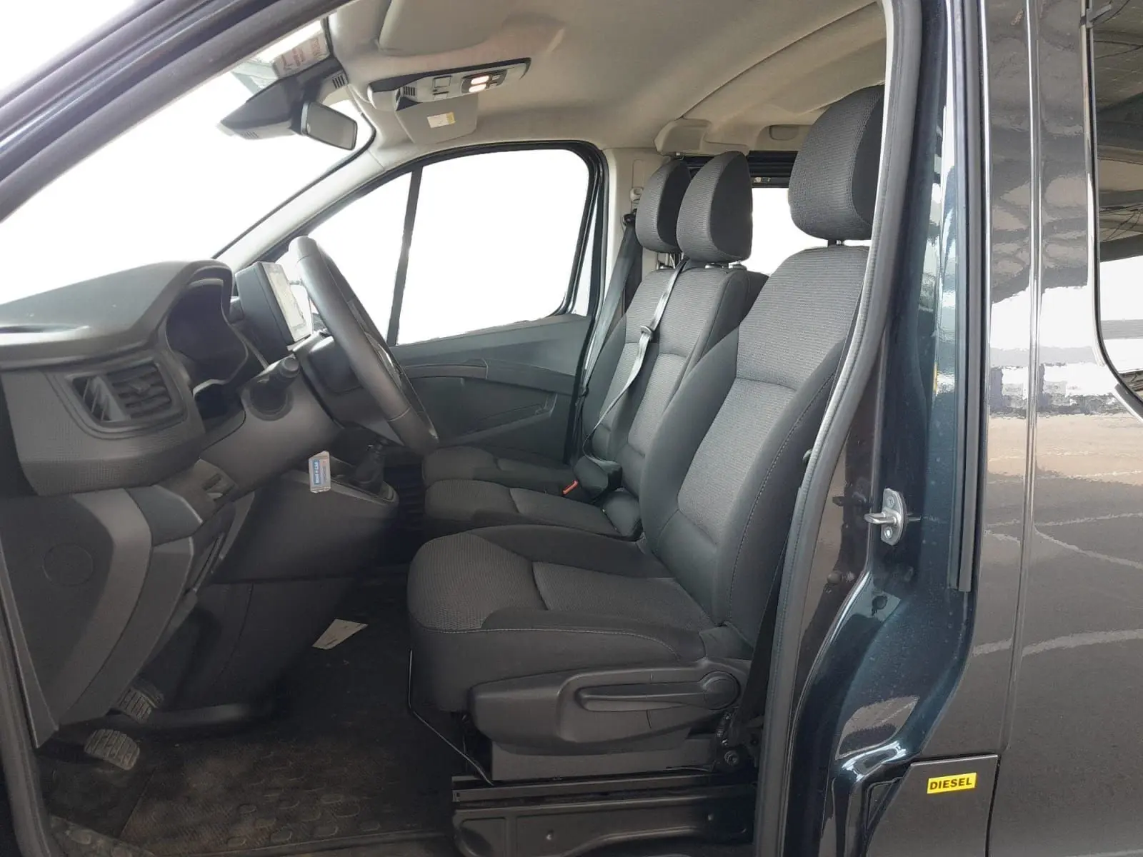 Vue intérieure côté conducteur du Renault Trafic Combi gris foncé, montrant les sièges avant et le tableau de bord.