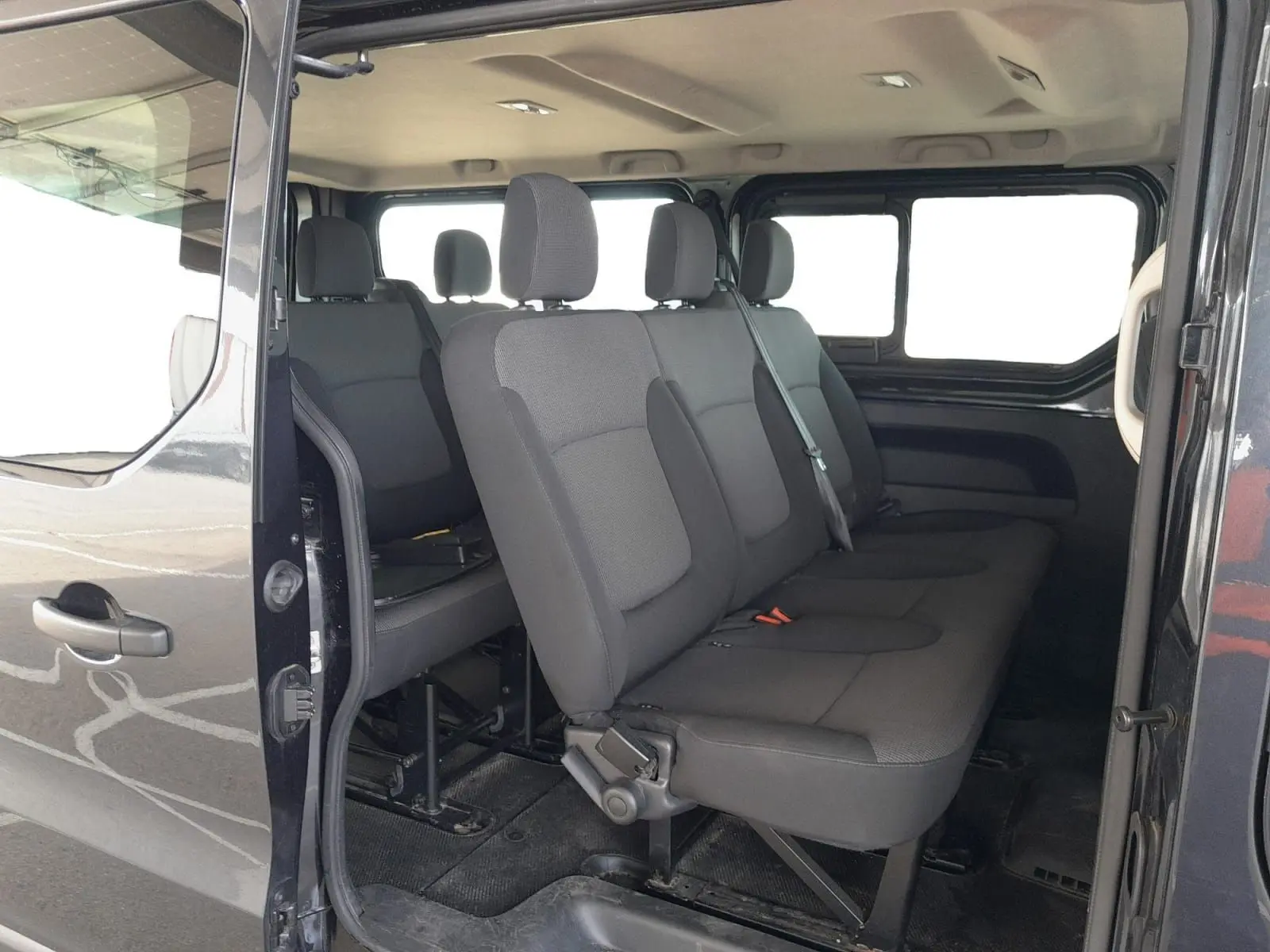 Vue intérieure côté droit du Renault Trafic Combi gris foncé, montrant les sièges passagers en tissu noir sur trois rangées.