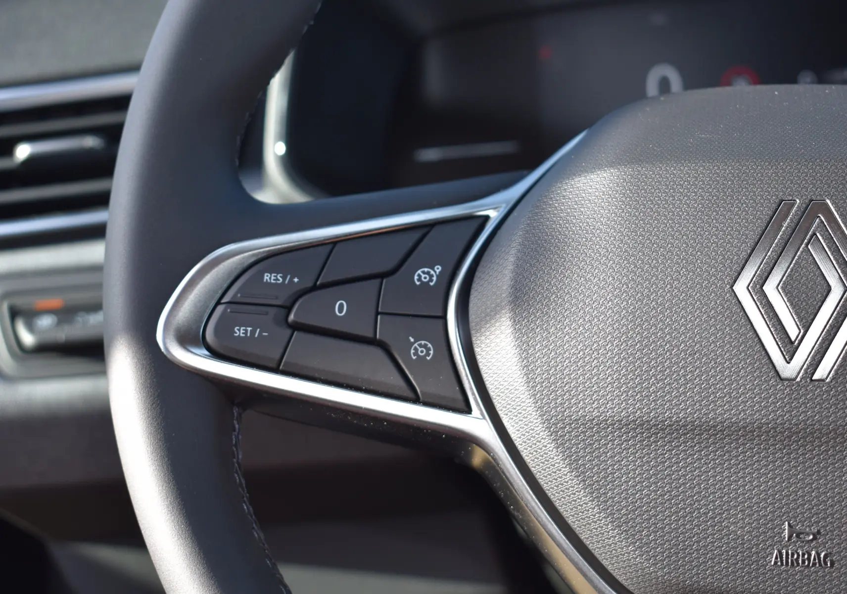 Gros plan sur le volant noir de la Renault Clio V 2025, avec commandes de régulateur de vitesse et logo Renault central.