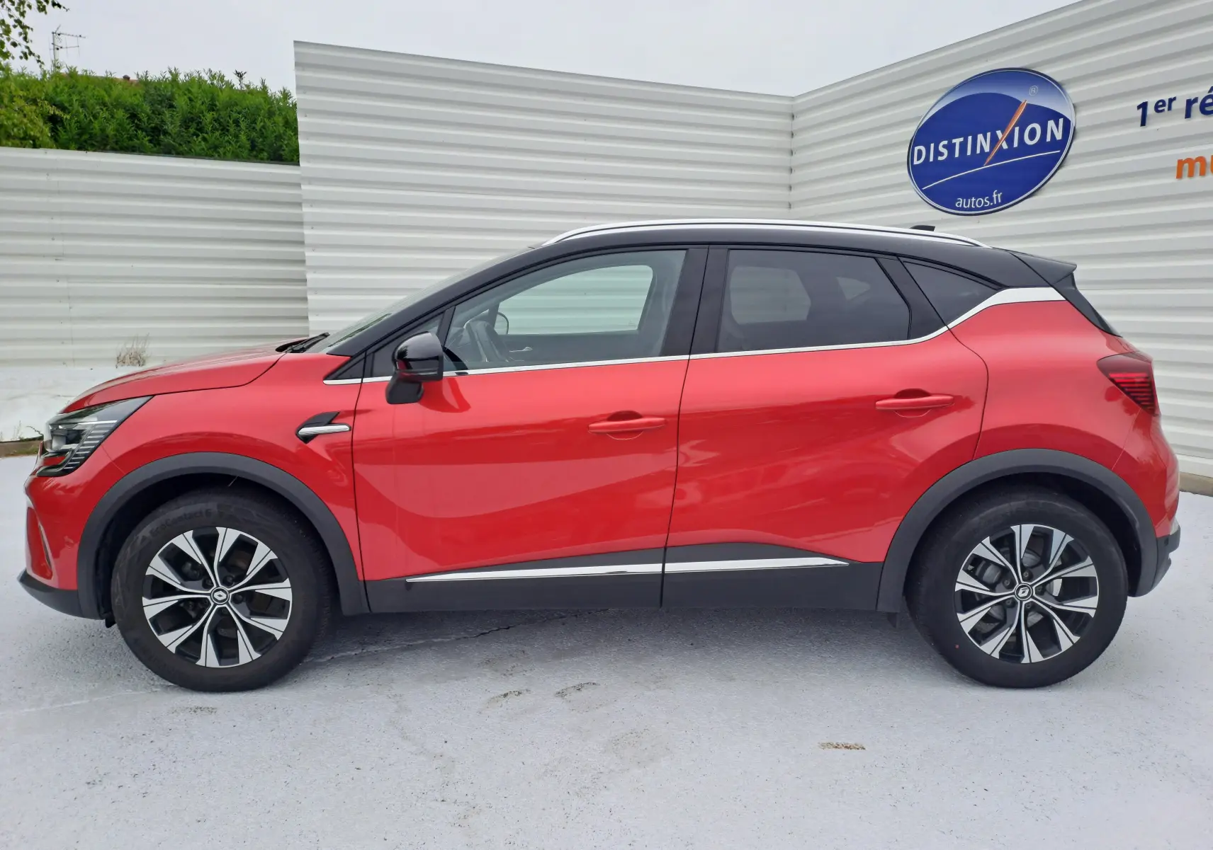 Profil côté gauche d'un Renault Captur 2024 rouge flamme métal avec toit noir et jantes alliage bicolores.