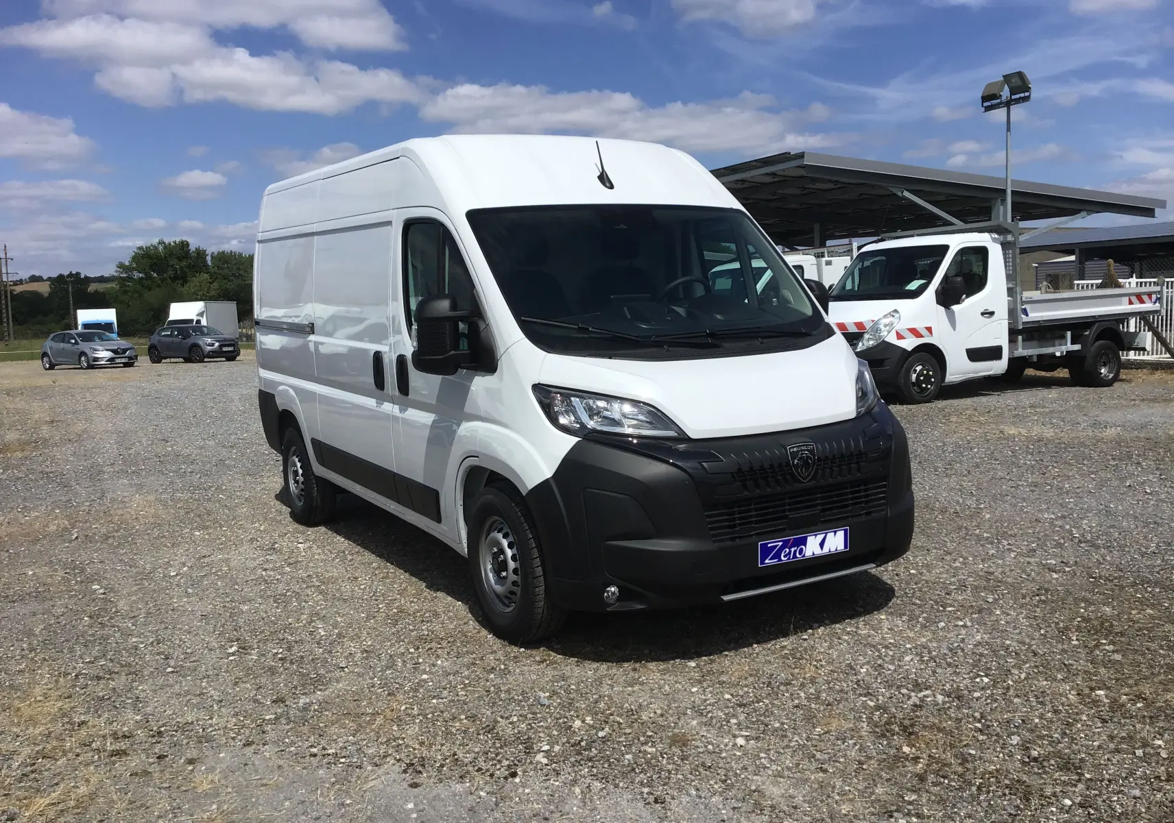 Fourgon PEUGEOT BOXER blanc en 3/4 avant droit sur un parking, avec calandre noire et logo visible.