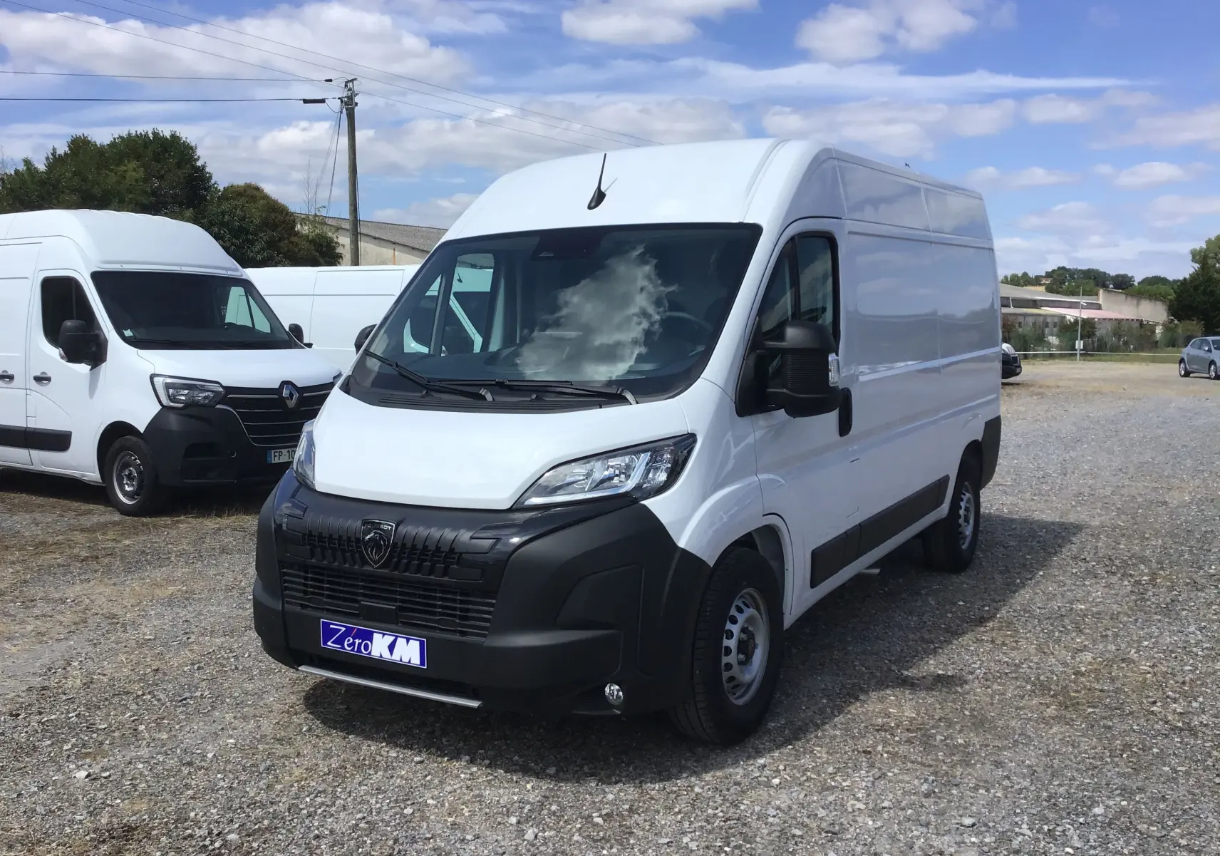 Fourgon PEUGEOT BOXER blanc en 3/4 avant droit sur un terrain extérieur avec plusieurs autres utilitaires blancs en arrière-plan.