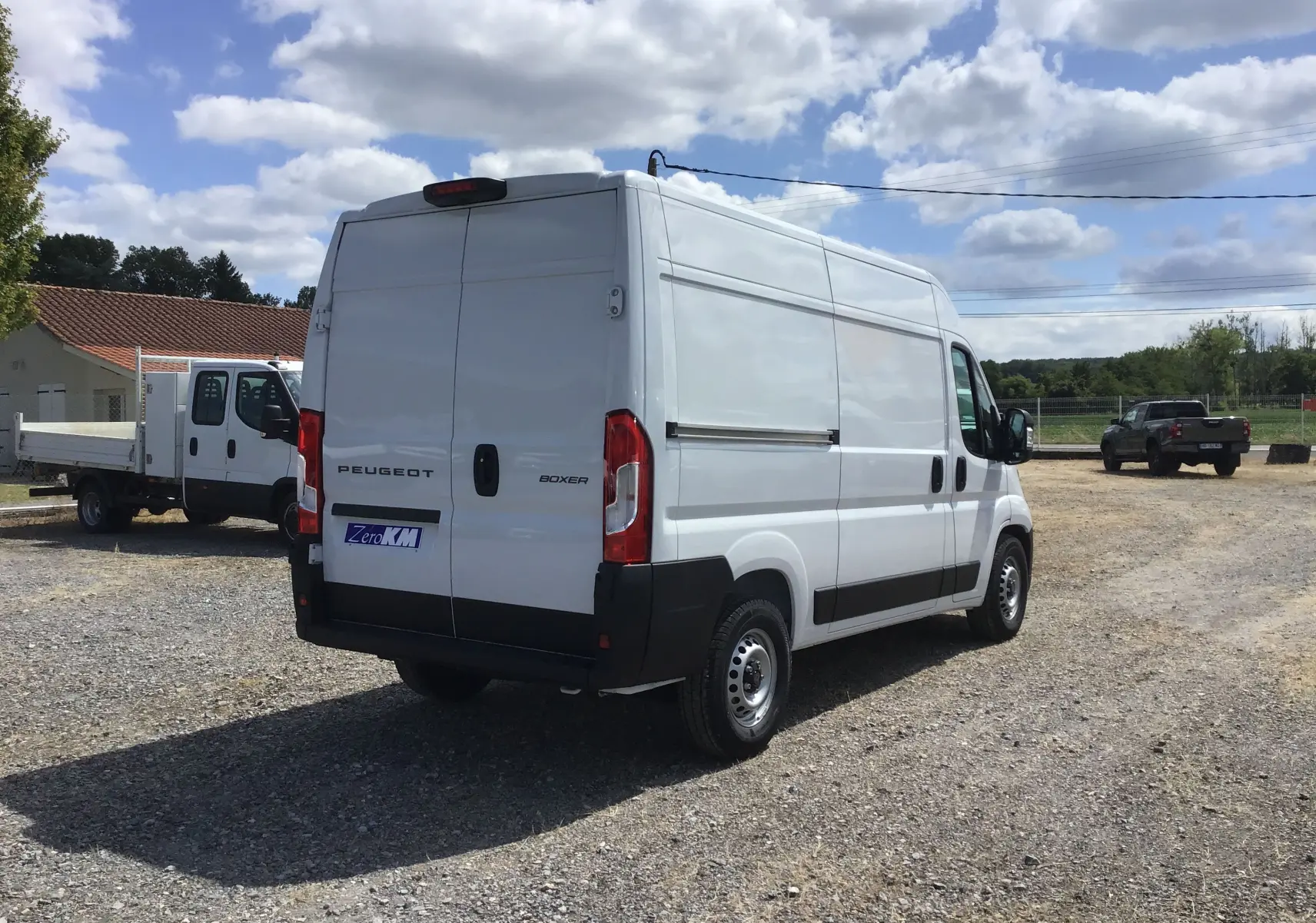 Vue 3/4 arrière droite d'un utilitaire Peugeot Boxer blanc L2H2 avec portes arrière fermées sur un parking extérieur.