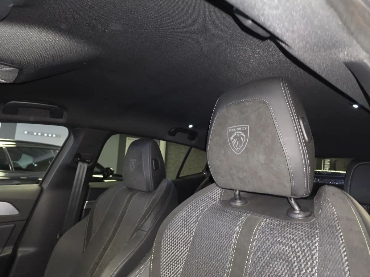 Gros plan sur les sièges avant gris avec appuis-tête brodés du lion Peugeot dans l’habitacle sombre de la 408 GT 2025.