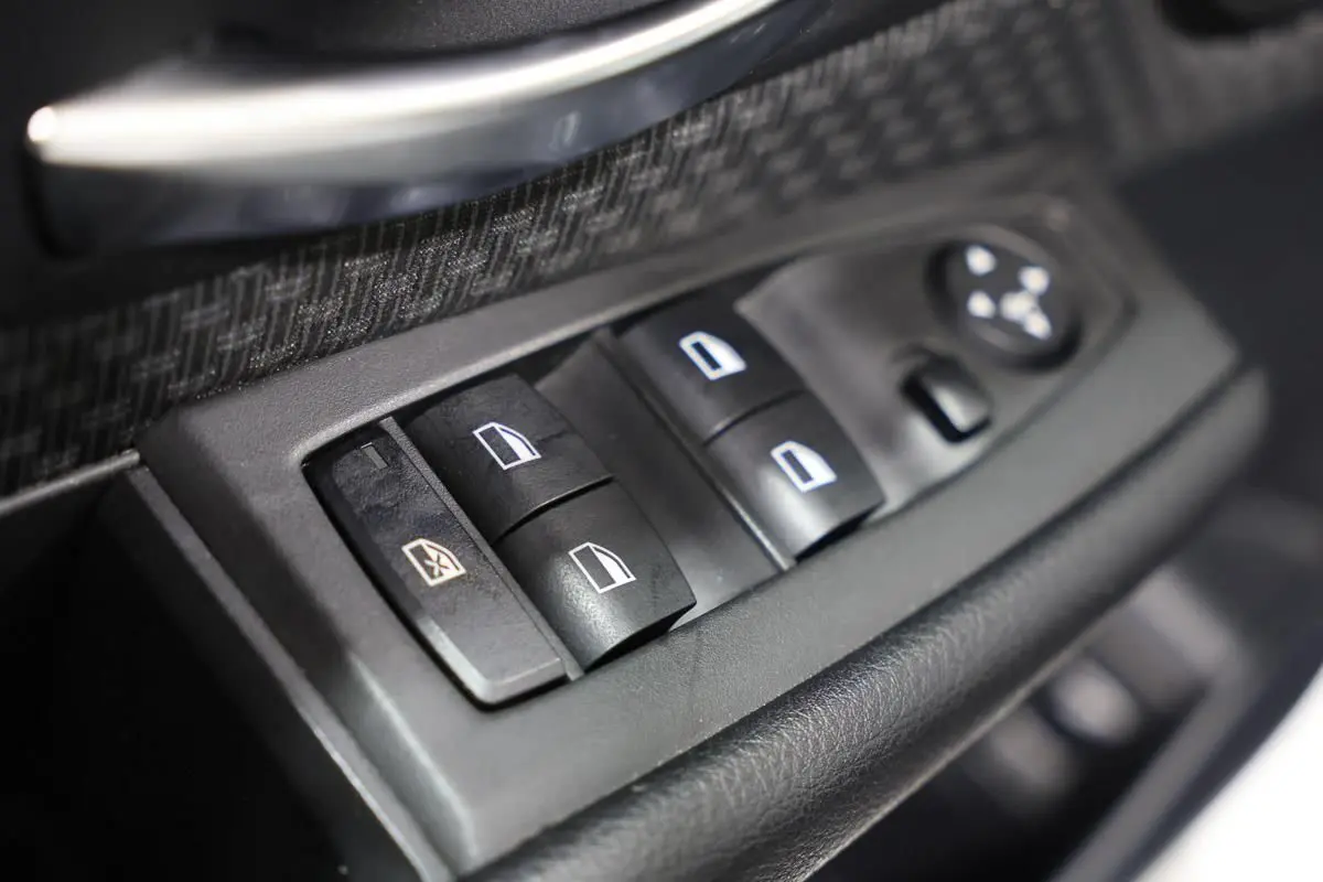 Gros plan sur les commandes des vitres électriques côté conducteur d'une BMW Série 2 Active Tourer blanche, intérieur noir.