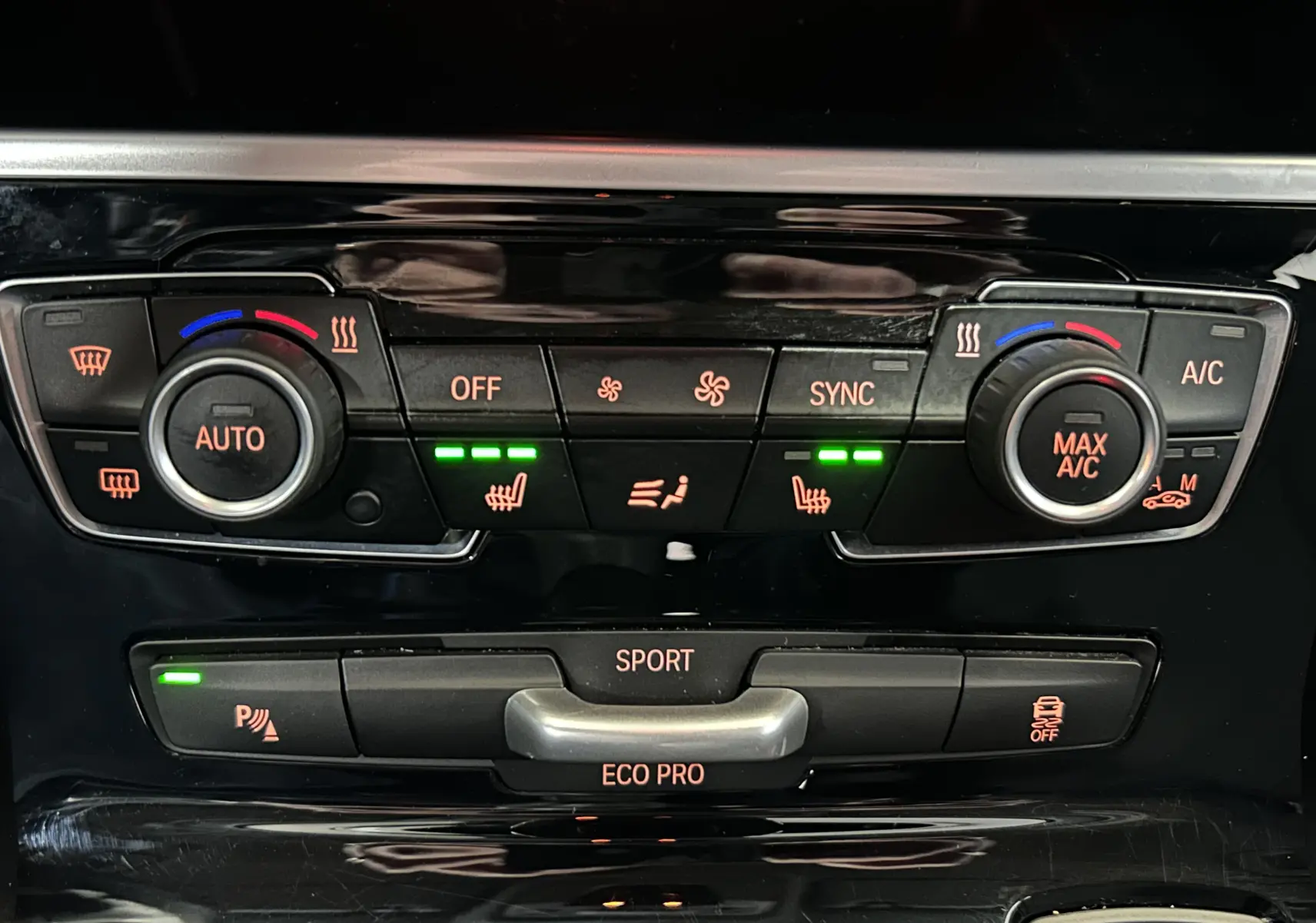 Gros plan sur la console centrale de la BMW Série 2 Active Tourer blanche, avec commandes climatisation et sièges chauffants activés.