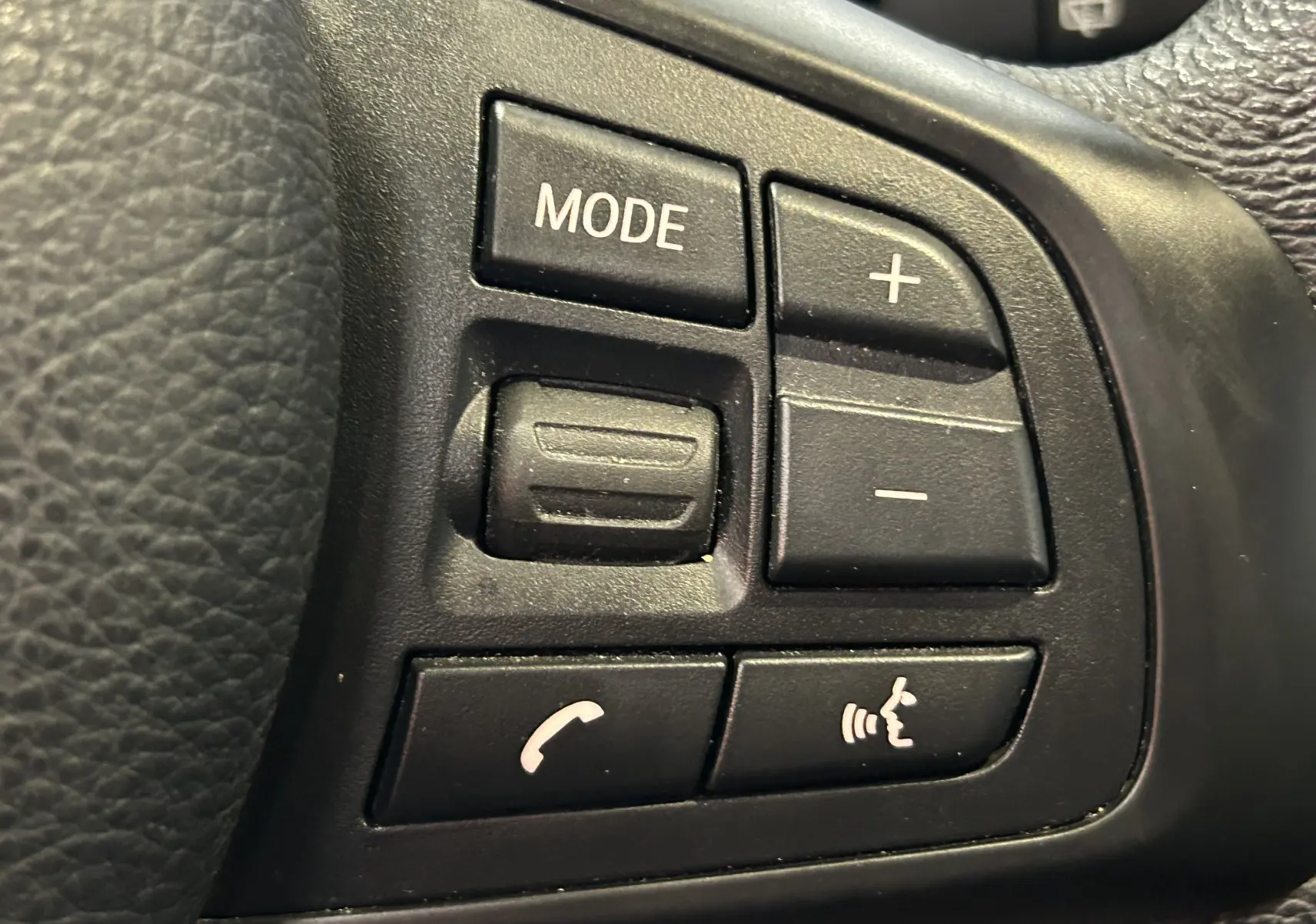Gros plan sur les commandes multifonctions noires du volant d’une BMW Série 2 Active Tourer blanche de 2021.