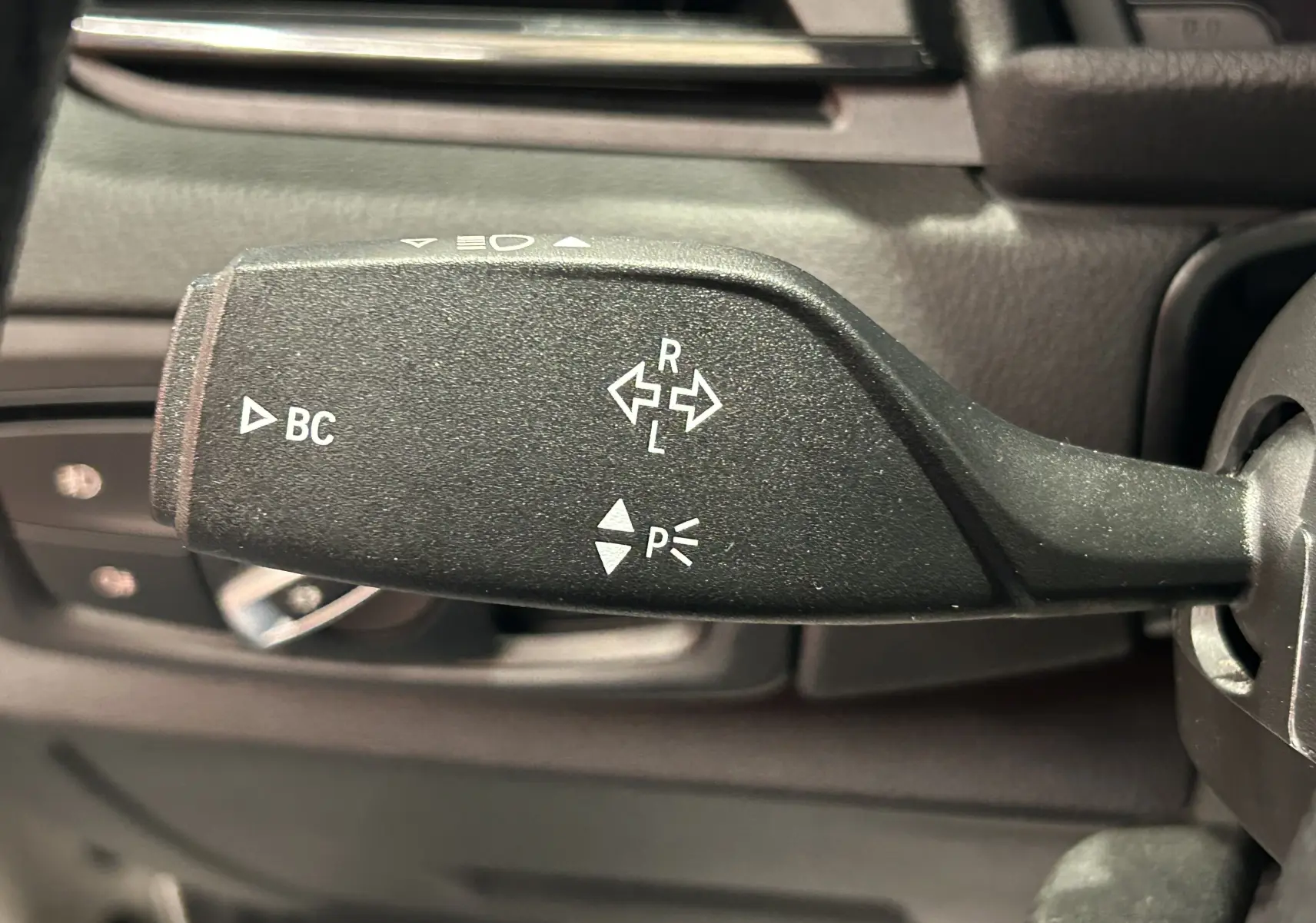 Gros plan sur la commande de clignotant à gauche du volant dans l'habitacle d'une BMW Série 2 Active Tourer blanche.