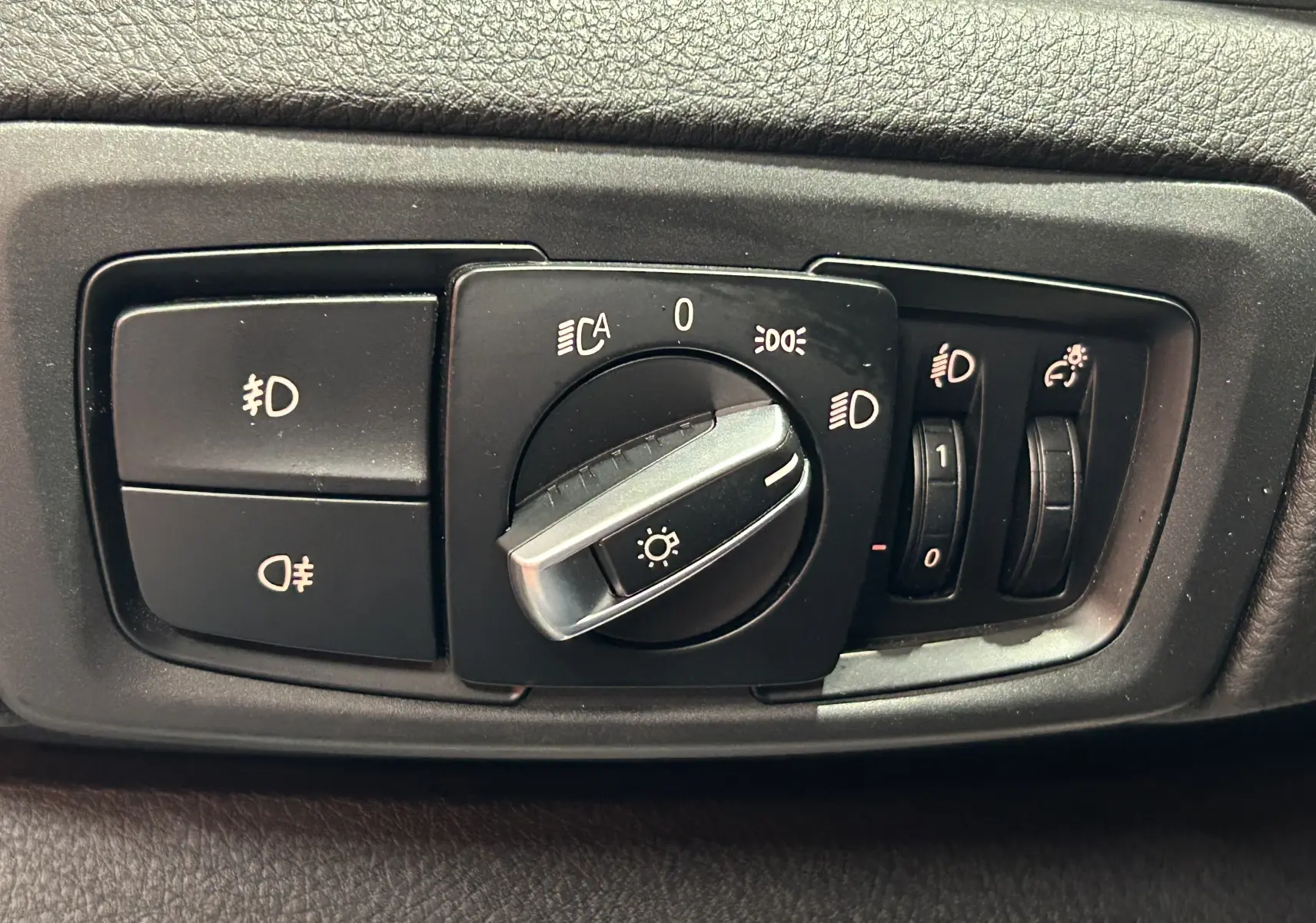 Gros plan sur le bouton de commande des phares d'une BMW Série 2 Active Tourer blanche, intérieur noir.