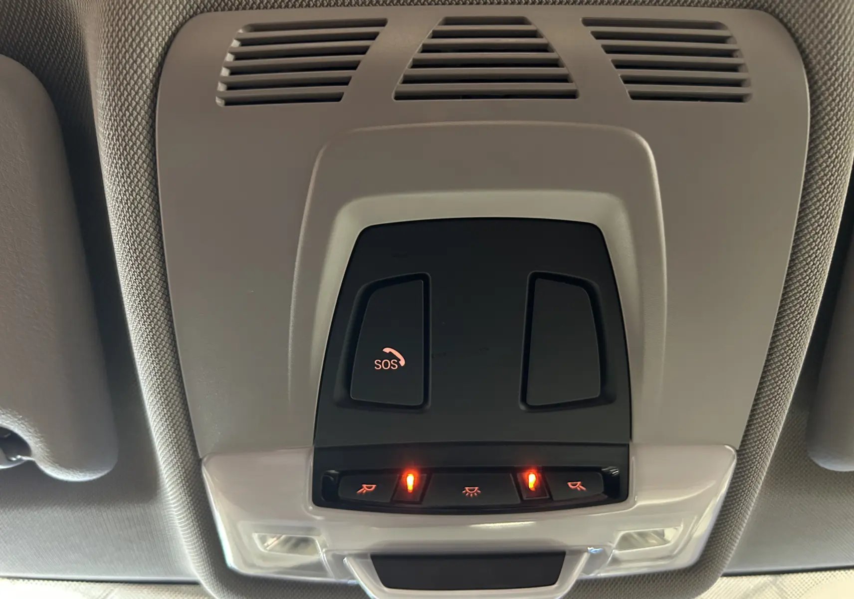 Vue en gros plan du panneau de commandes au plafond intérieur de la BMW Série 2 Active Tourer blanc, avec bouton SOS et éclairage activé.