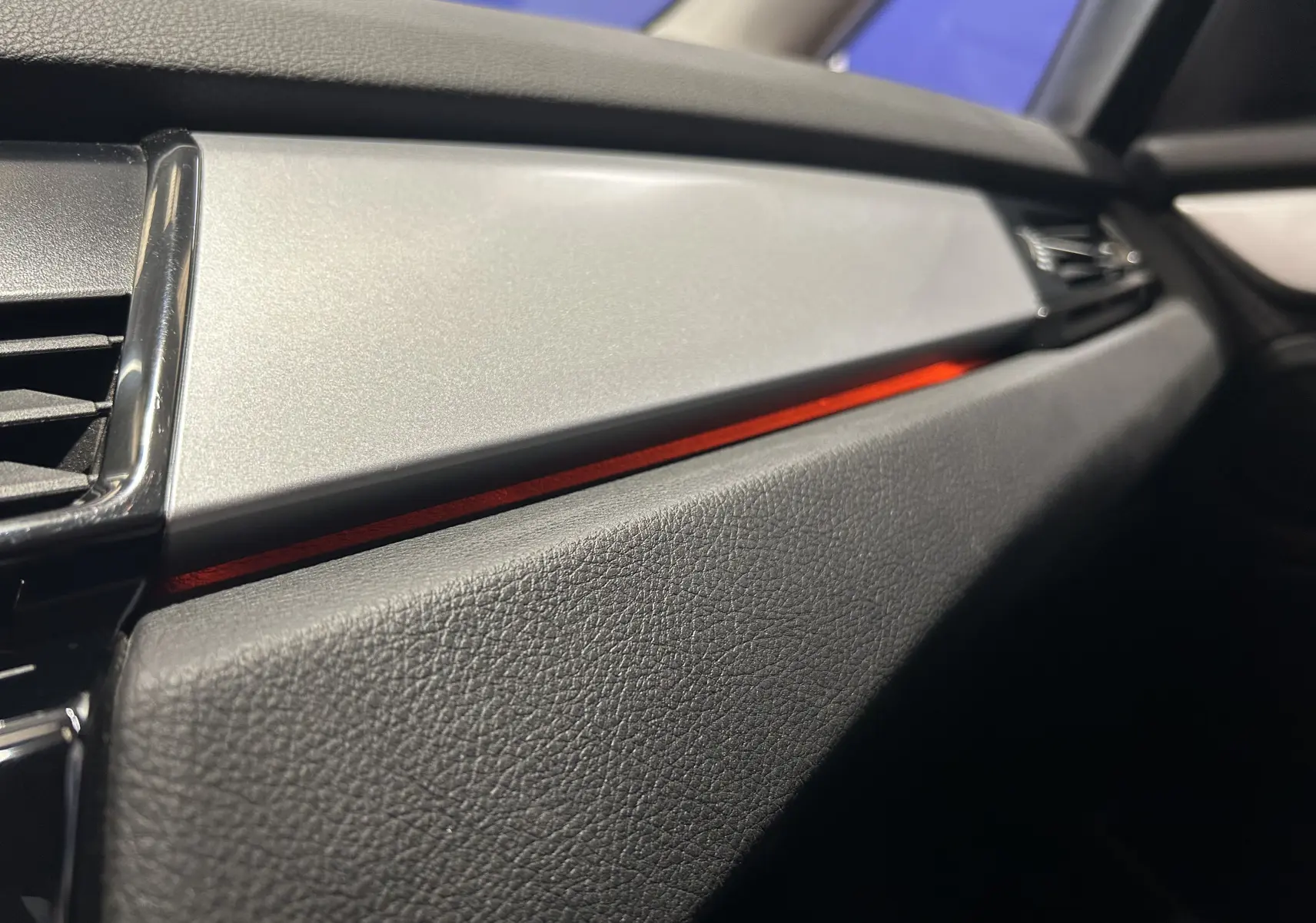 Détail intérieur côté passager de la BMW Série 2 Active Tourer 216d 2021, avec bande décorative rouge et finition noire texturée.