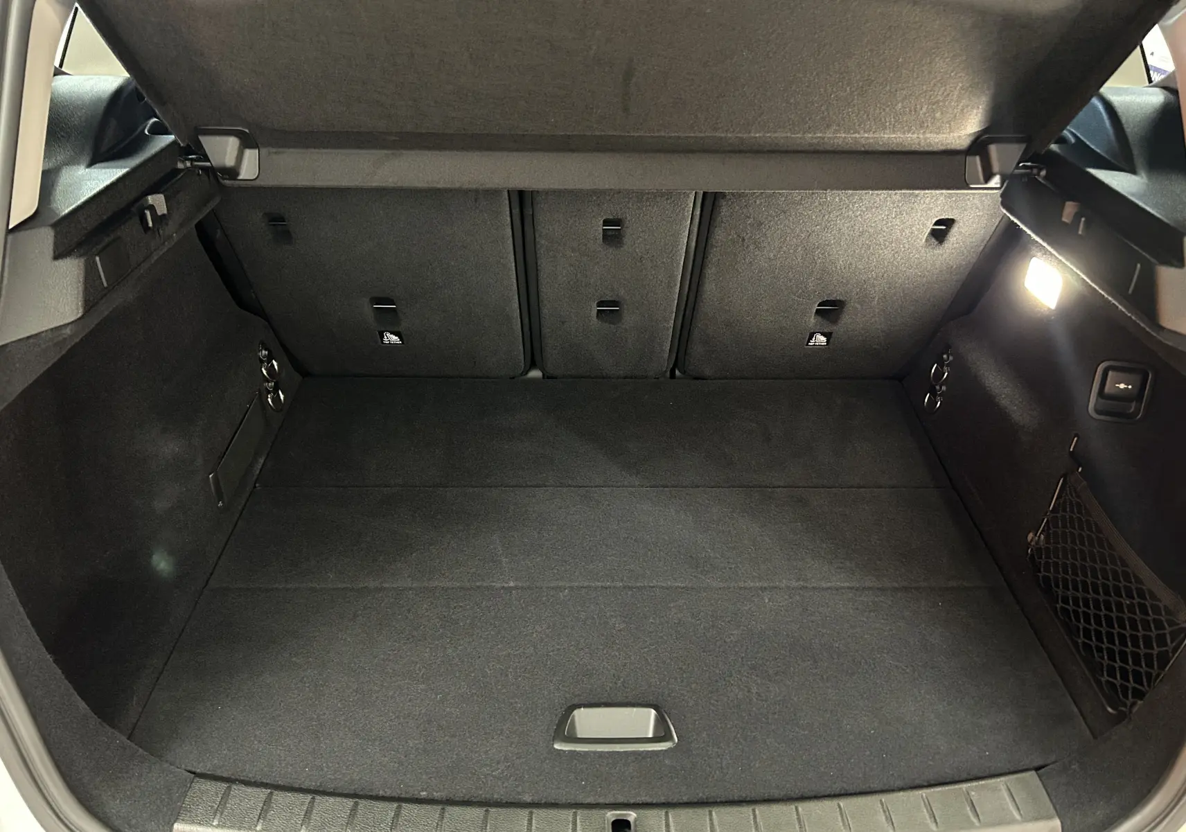 Vue intérieure du coffre spacieux et propre de la BMW Série 2 Active Tourer 216d, avec éclairage latéral allumé.