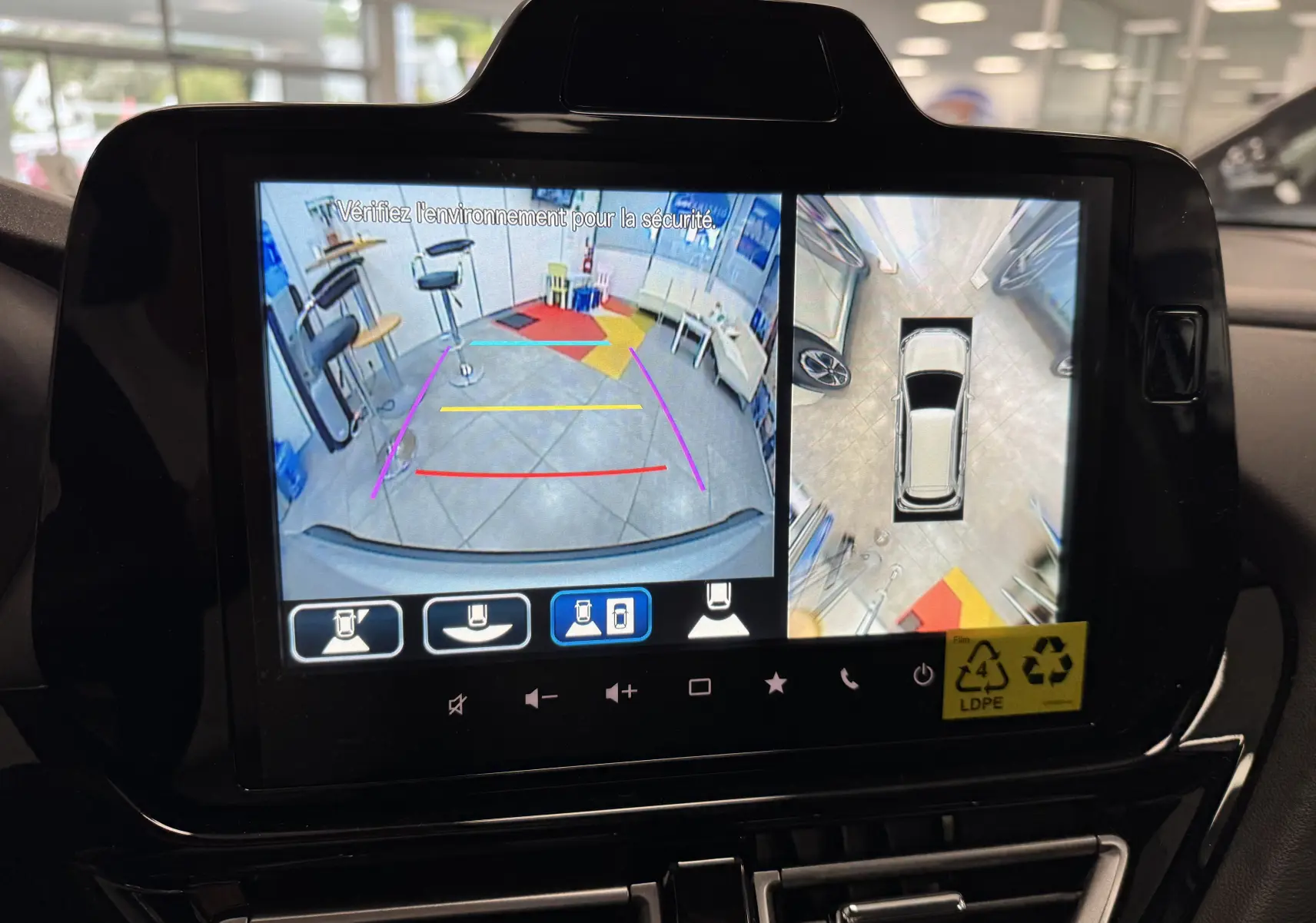 Écran multimédia montrant la caméra de recul et vue à 360° du Suzuki S-Cross gris en stationnement intérieur.