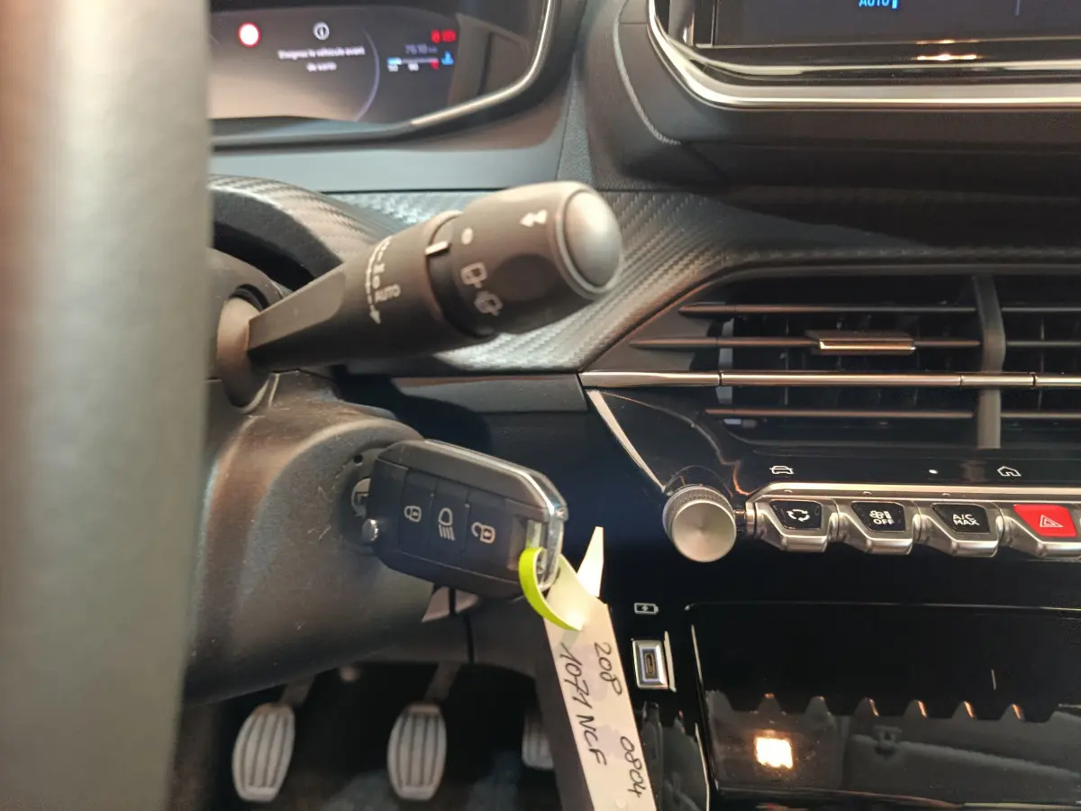 Gros plan intérieur côté gauche sur le tableau de bord et clé insérée d'une Peugeot 208 gris clair 2025 PureTech Allure