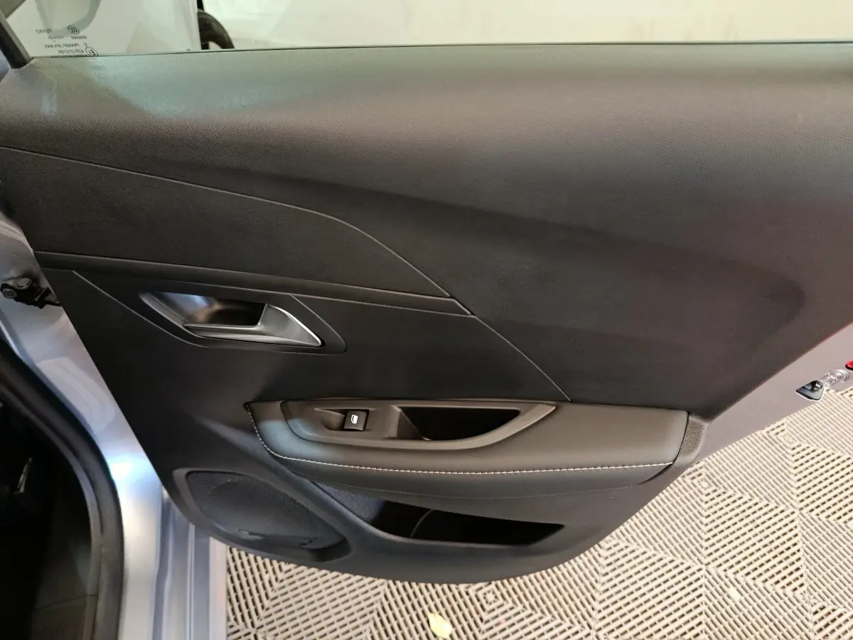 Vue rapprochée de la porte avant gauche gris clair du Peugeot 208 PureTech 100 S&S Allure avec poignée et commande de vitre.