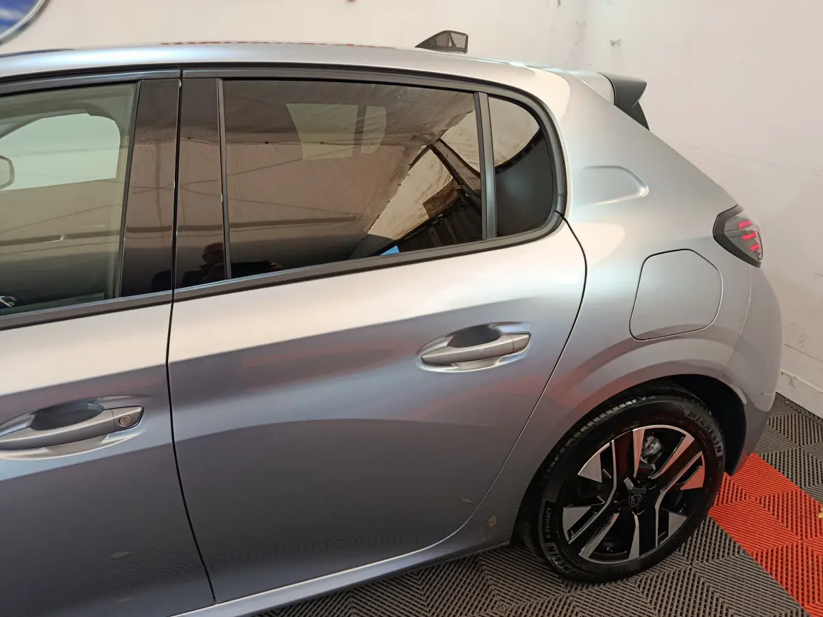 Vue latérale droite sur la partie arrière d'une Peugeot 208 gris clair avec jante noire et détails de porte visibles.