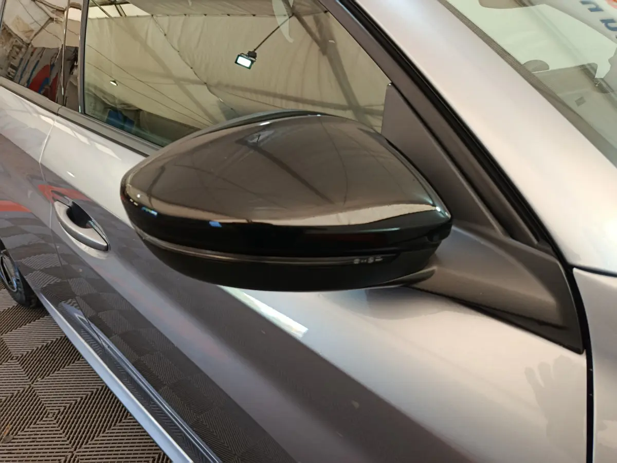 Gros plan sur le rétroviseur droit noir brillant d'une Peugeot 208 gris clair, vue côté conducteur.