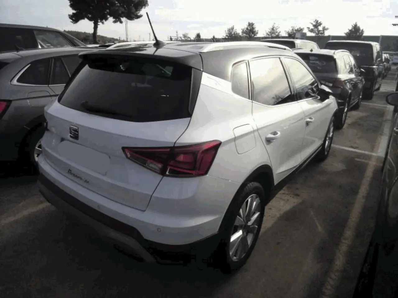 Vue 3/4 arrière droite d'un SEAT Arona blanc Nevada avec toit noir et vitres arrière surteintées, garé en extérieur.