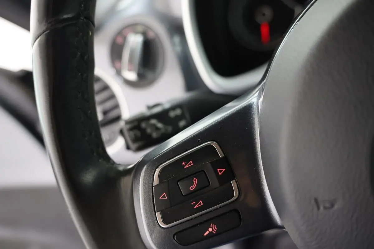 Gros plan sur les commandes au volant en cuir noir de la Volkswagen Coccinelle 2016, avec boutons rétroéclairés rouges.