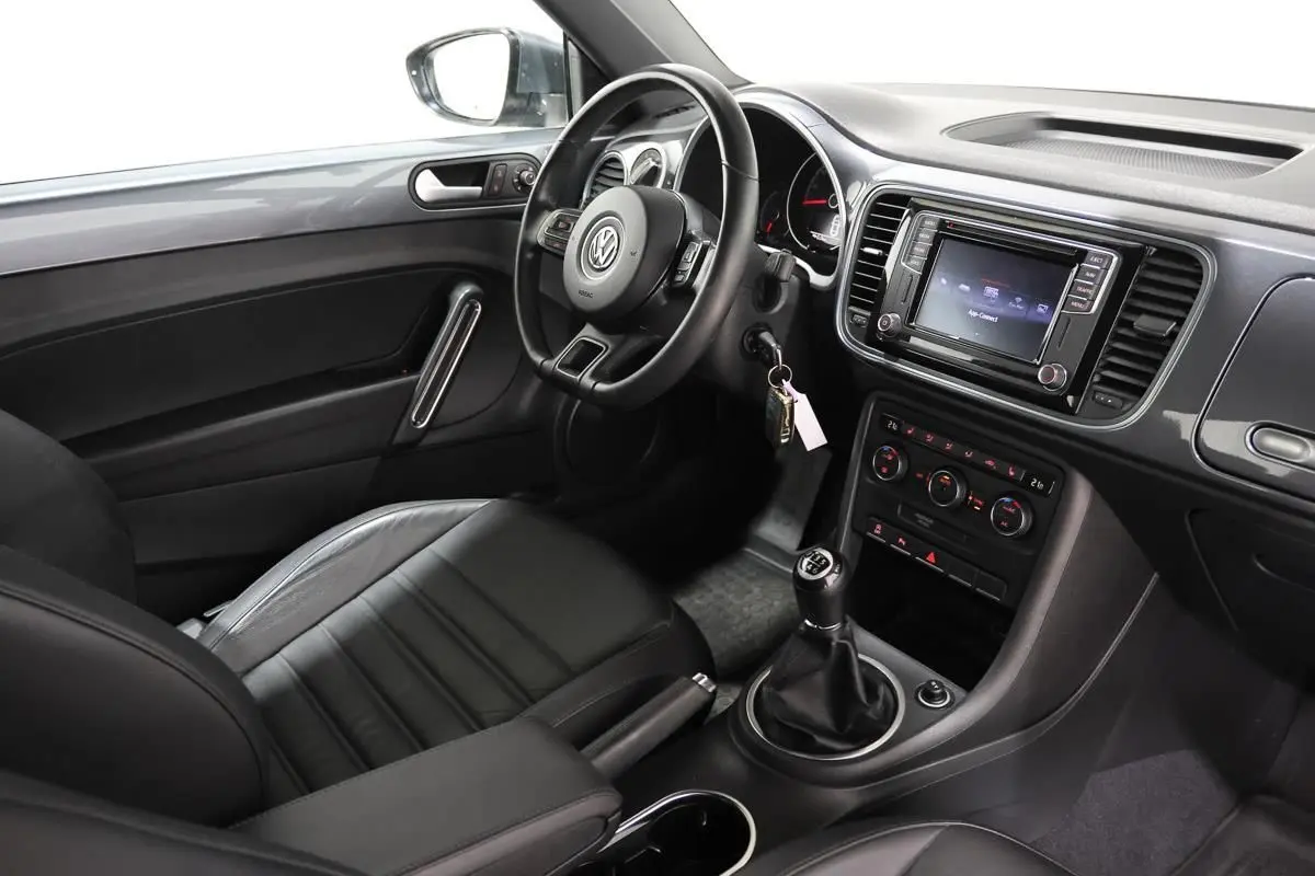 Intérieur côté conducteur de la Volkswagen Coccinelle gris 2016, volant cuir, GPS et boîte manuelle visibles.
