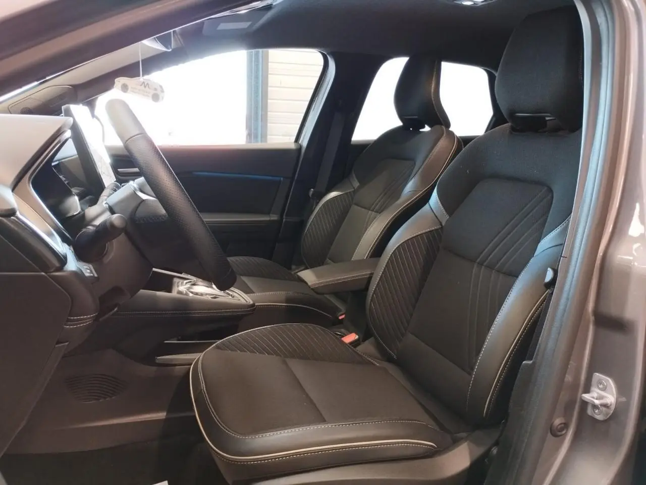 Vue intérieure côté gauche du Renault Symbioz 2025 gris Cassiope, montrant les sièges avant en tissu noir avec surpiqûres claires.