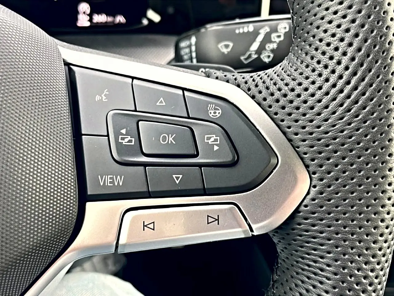 Gros plan sur les commandes multifonctions en plastique noir et argent du volant perforé côté gauche d’une Volkswagen Golf noire.