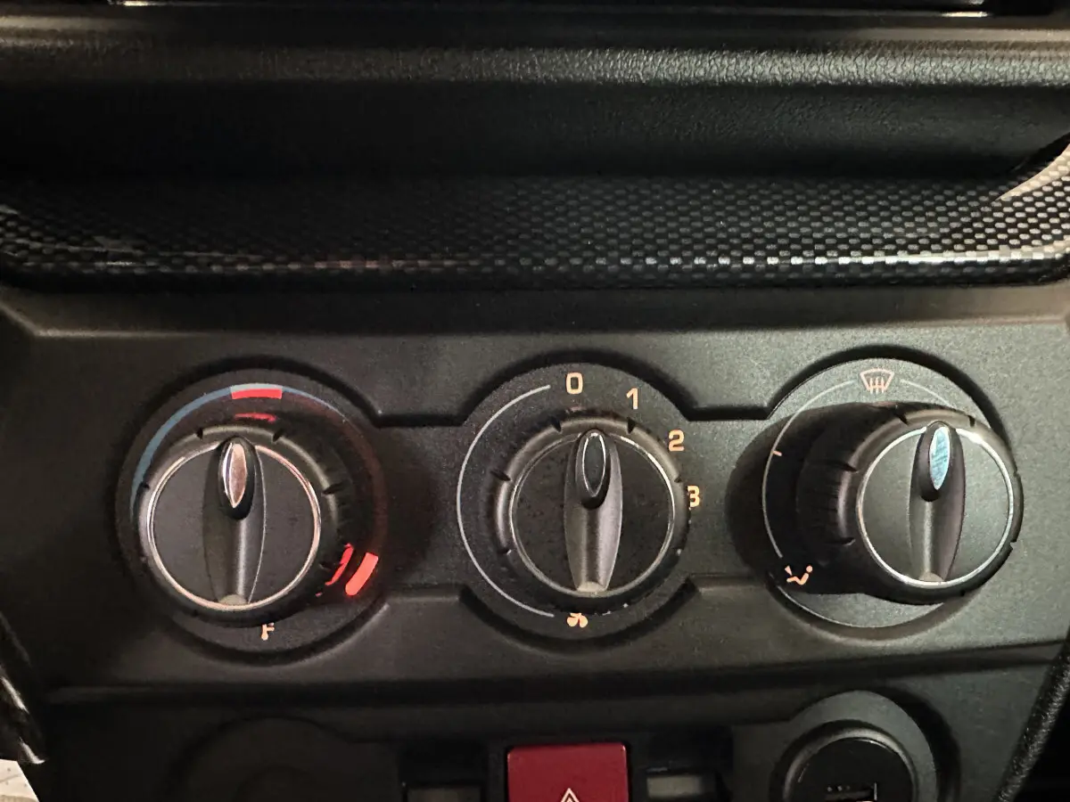 Gros plan sur les commandes de climatisation noires d'une Aixam Ambition rouge, avec réglages de température, ventilation et désembuage.