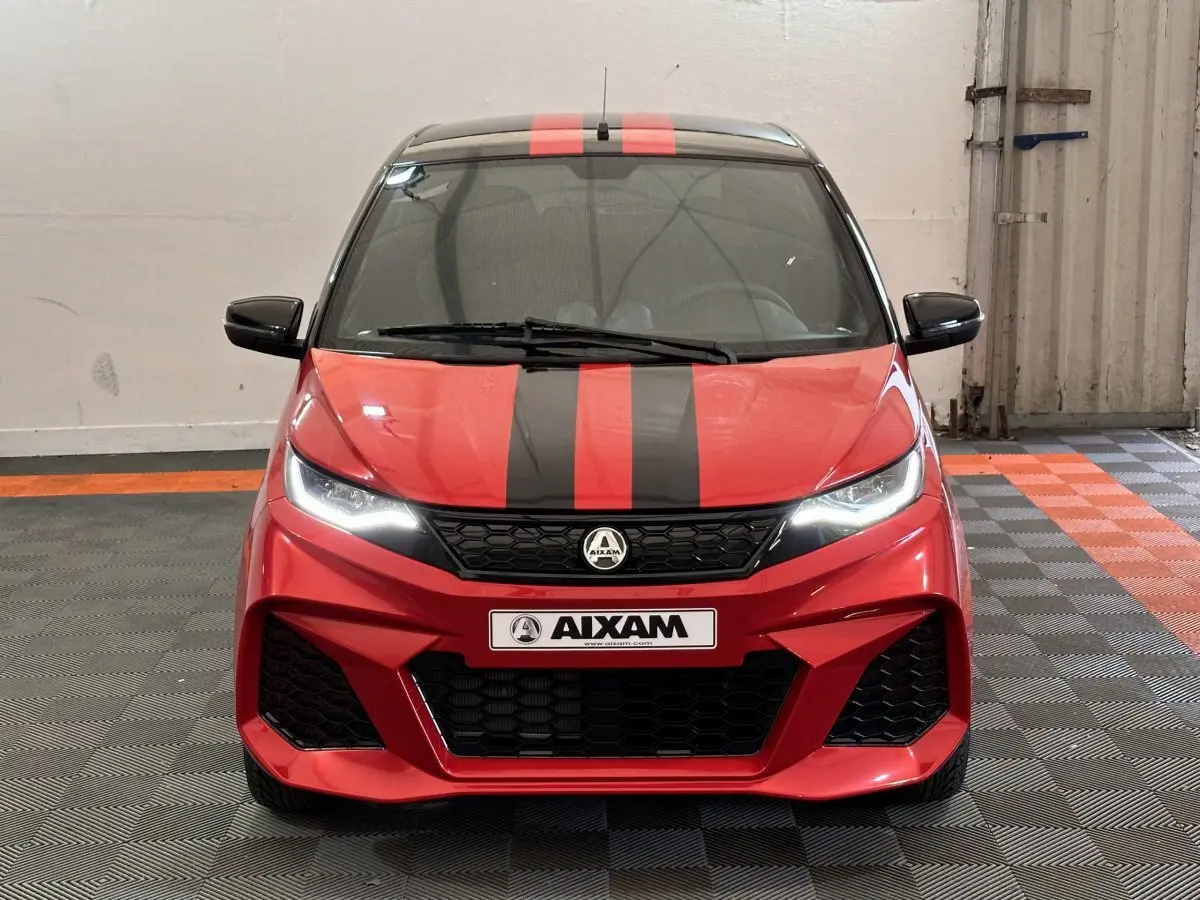 Vue avant d'une Aixam Ambition 0.5 City Coupe GTI rouge avec bandes noires et rétroviseur caméra côté conducteur.