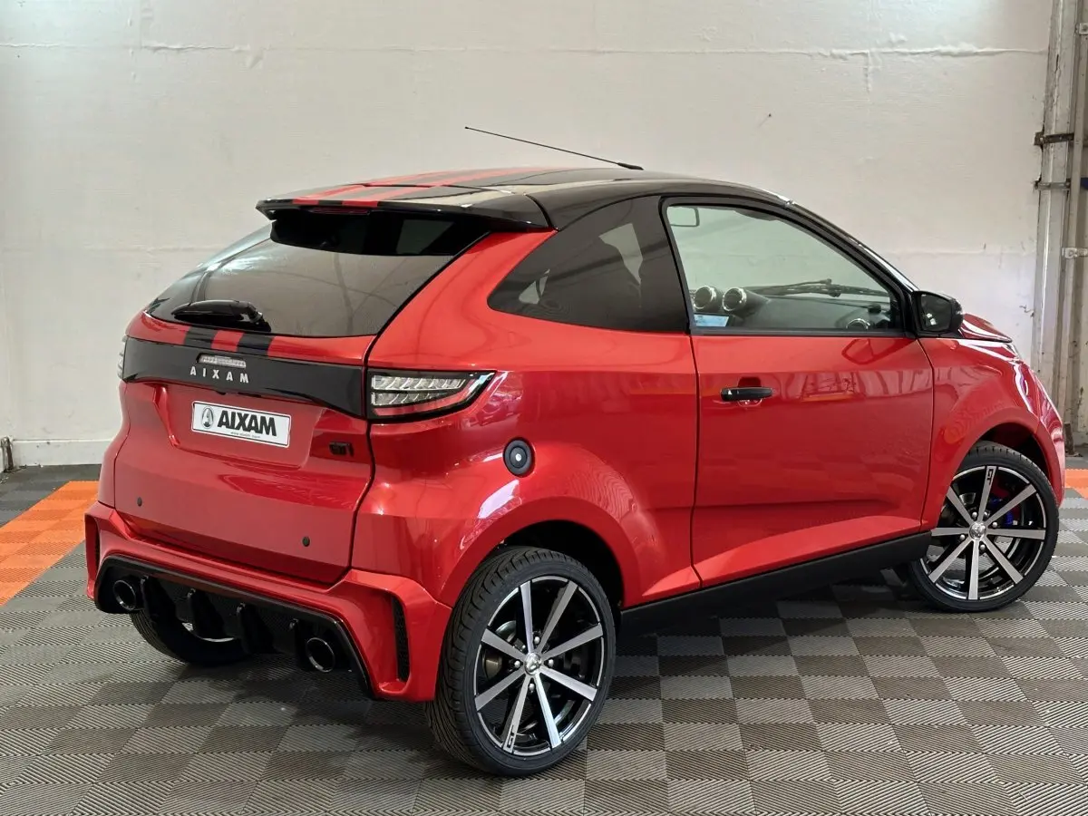 Vue 3/4 arrière droite de l'AIXAM AMBITION 0.5 CITY COUPE GTI rouge avec toit noir et jantes sport.