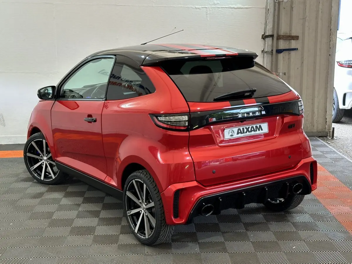 Vue 3/4 arrière droite de l'AIXAM Ambition rouge 2026 avec bandes noires, jantes sport et rétroviseur caméra côté gauche.