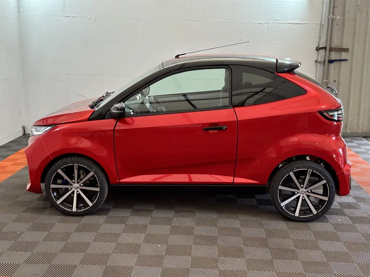 Vue de profil côté gauche d'une Aixam Ambition 0.5 City Coupe GTI rouge avec jantes noires et toit noir.