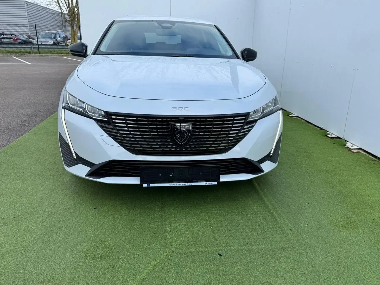 Vue frontale d'une Peugeot 308 SW blanche Okenite avec calandre noire et feux LED verticaux distinctifs.