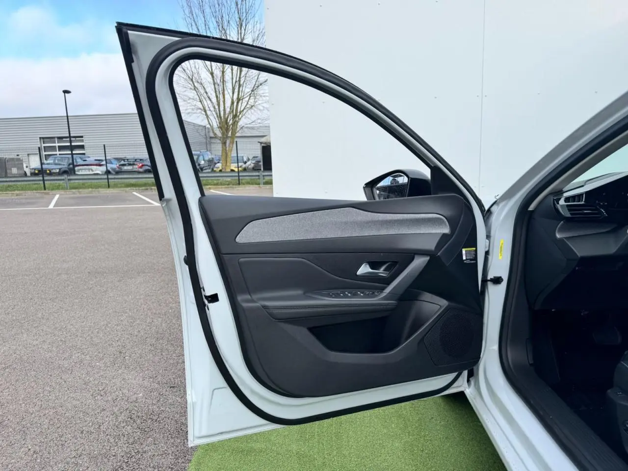 Porte avant gauche ouverte d'une Peugeot 308 SW blanche, montrant la garniture intérieure noire avec insert gris.
