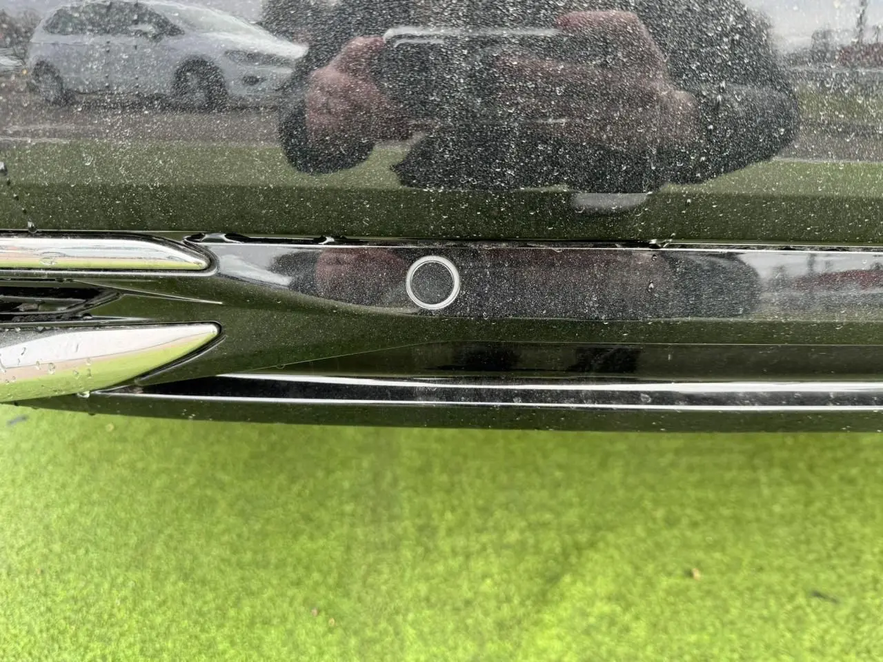 Gros plan sur le capteur de stationnement arrière noir du Peugeot 308 SW blanc Okenite, avec reflet et herbe verte en dessous.