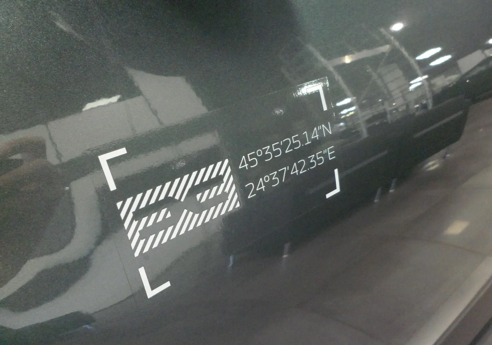 Gros plan sur l'autocollant "SS" avec coordonnées GPS sur la porte latérale droite d'un Dacia Jogger Vert Cèdre.