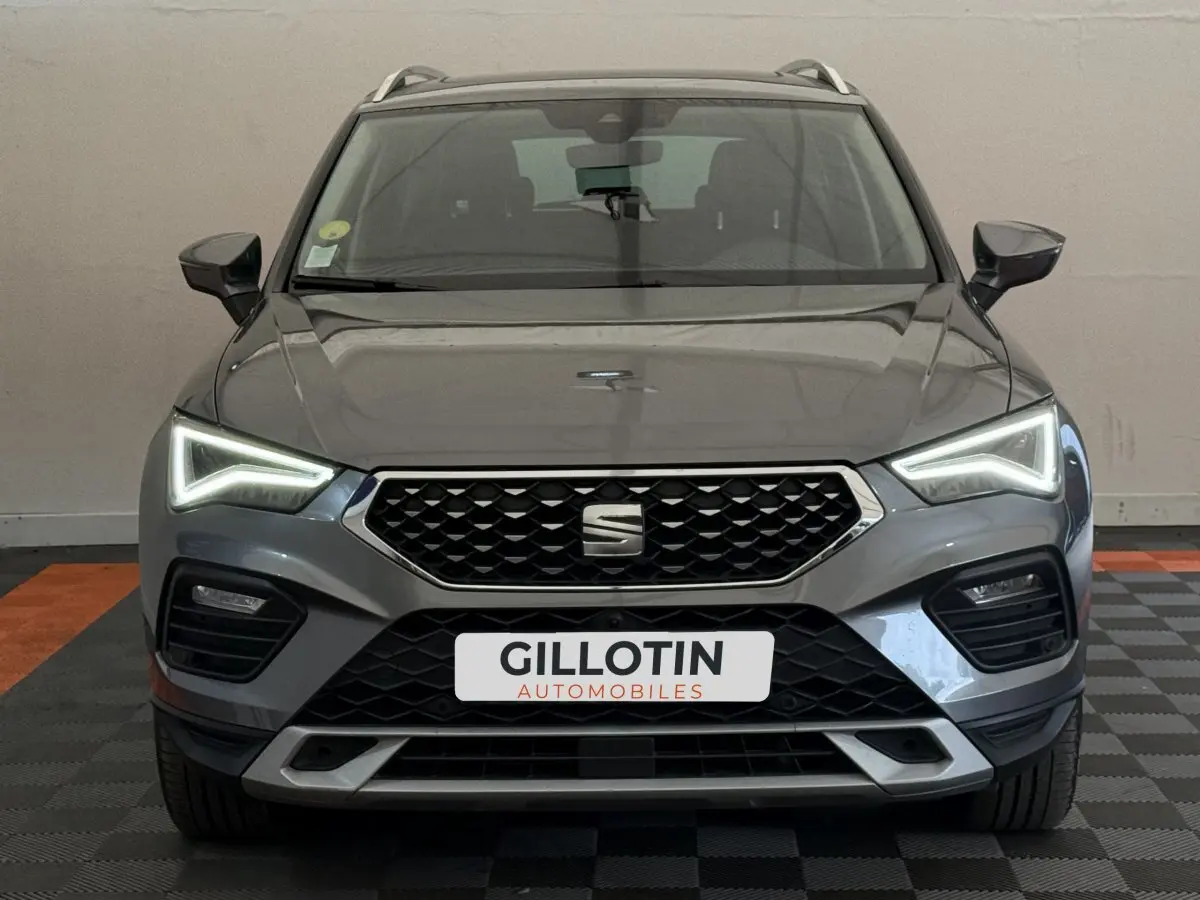 Vue frontale d'un SEAT Ateca gris clair 2023 avec phares LED allumés et calandre hexagonale noire.