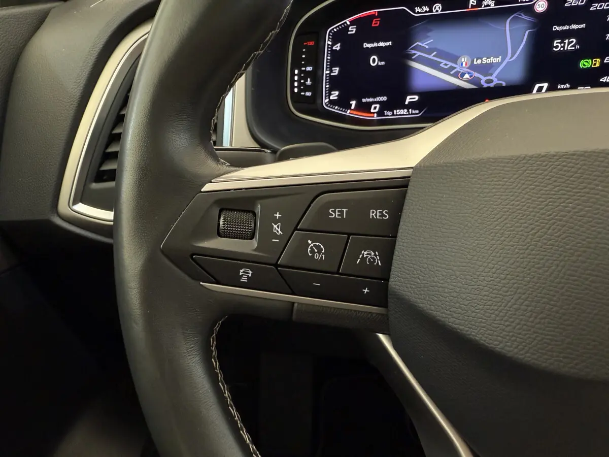 Vue rapprochée du volant cuir noir du SEAT Ateca 2023, avec commandes de régulateur et affichage numérique du tableau de bord.