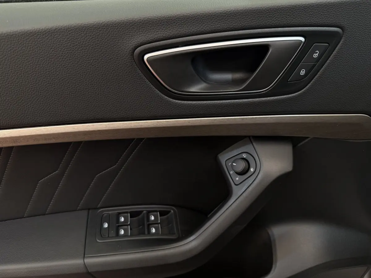 Gros plan sur la porte côté conducteur du SEAT Ateca gris clair, montrant la poignée, commandes vitres et réglage rétroviseurs.