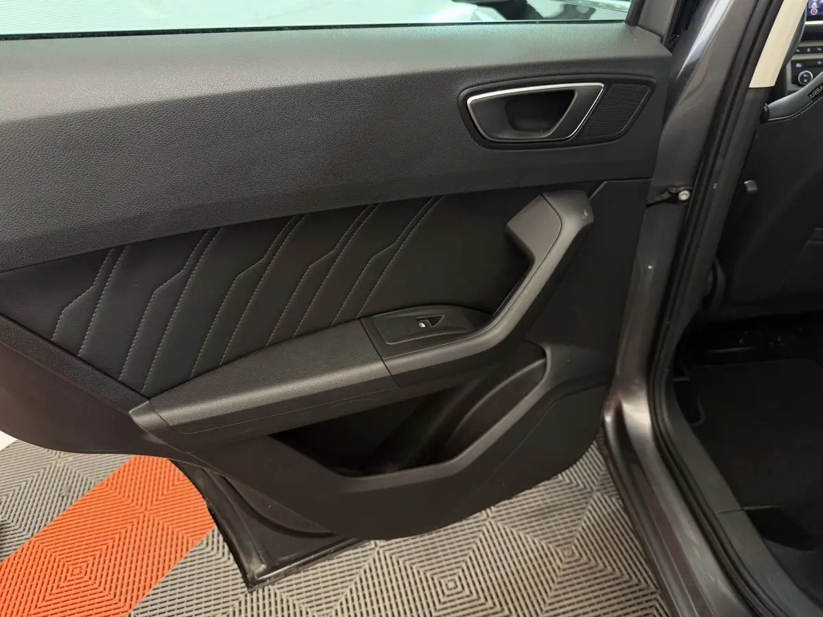 Vue intérieure du côté arrière gauche de la porte d’un SEAT Ateca gris clair, avec garniture en cuir noir et bouton de fenêtre électrique.