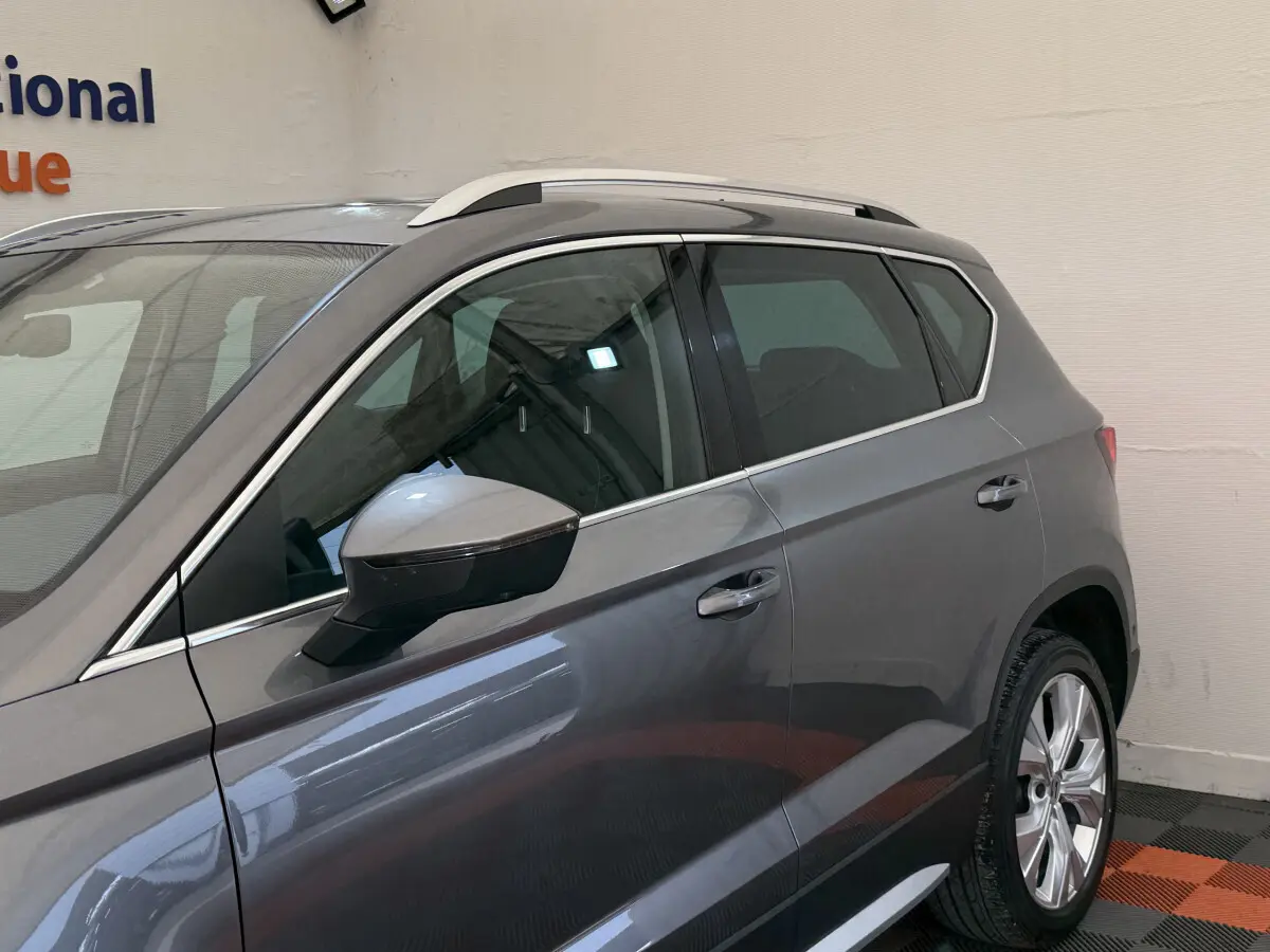 Vue latérale côté gauche d'un SEAT Ateca gris clair avec barres de toit chromées et jantes alliage.