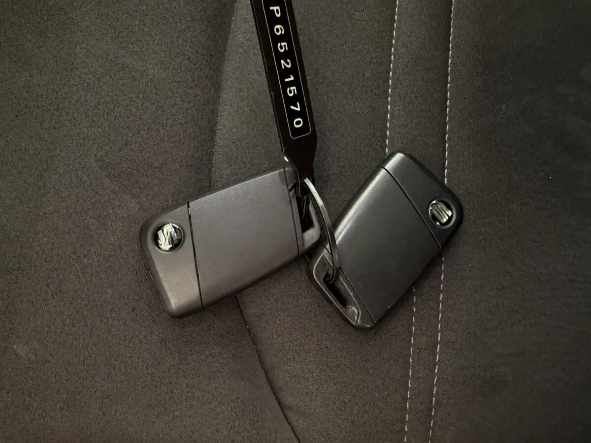 Gros plan sur deux clés noires SEAT posées sur une assise de siège en tissu gris foncé avec surpiqûres blanches.