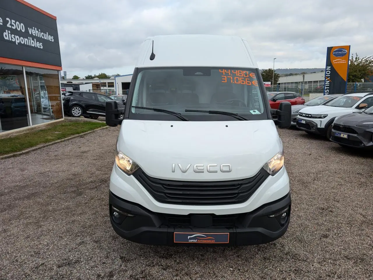 Vue de face d'un utilitaire Iveco Daily blanc avec calandre noire et phares allumés sur un parking.