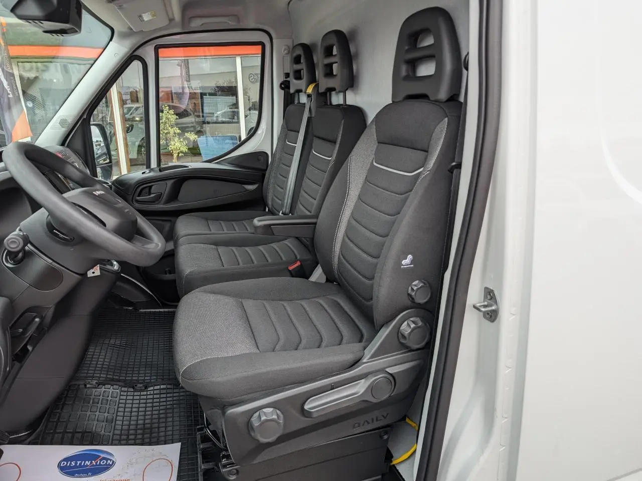 Intérieur côté conducteur du fourgon Iveco Daily blanc 2025, montrant les sièges en tissu gris et le tableau de bord noir.