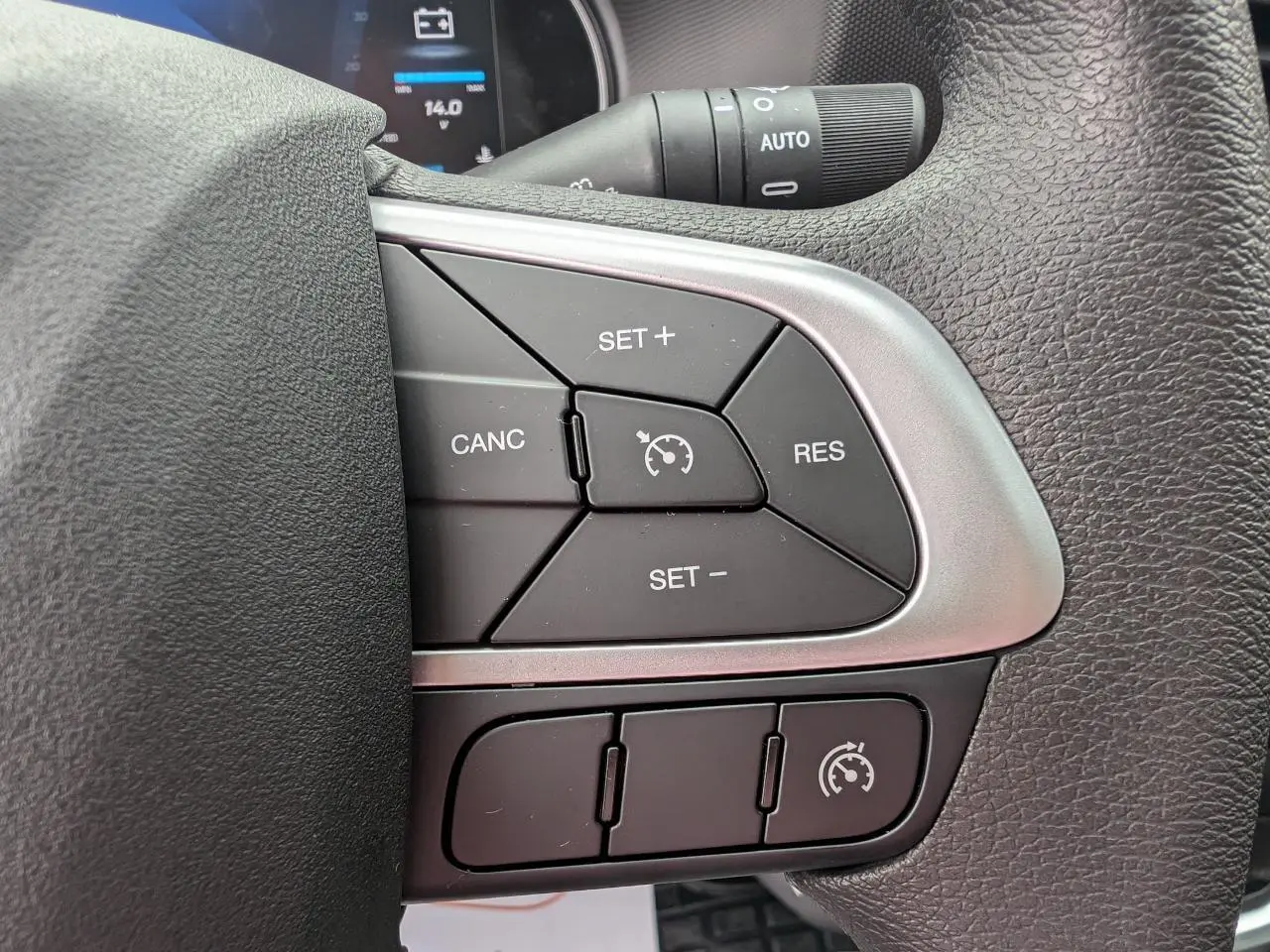 Gros plan sur les commandes du régulateur de vitesse au volant du Iveco Daily 35S16 blanc, tableau de bord en arrière-plan.